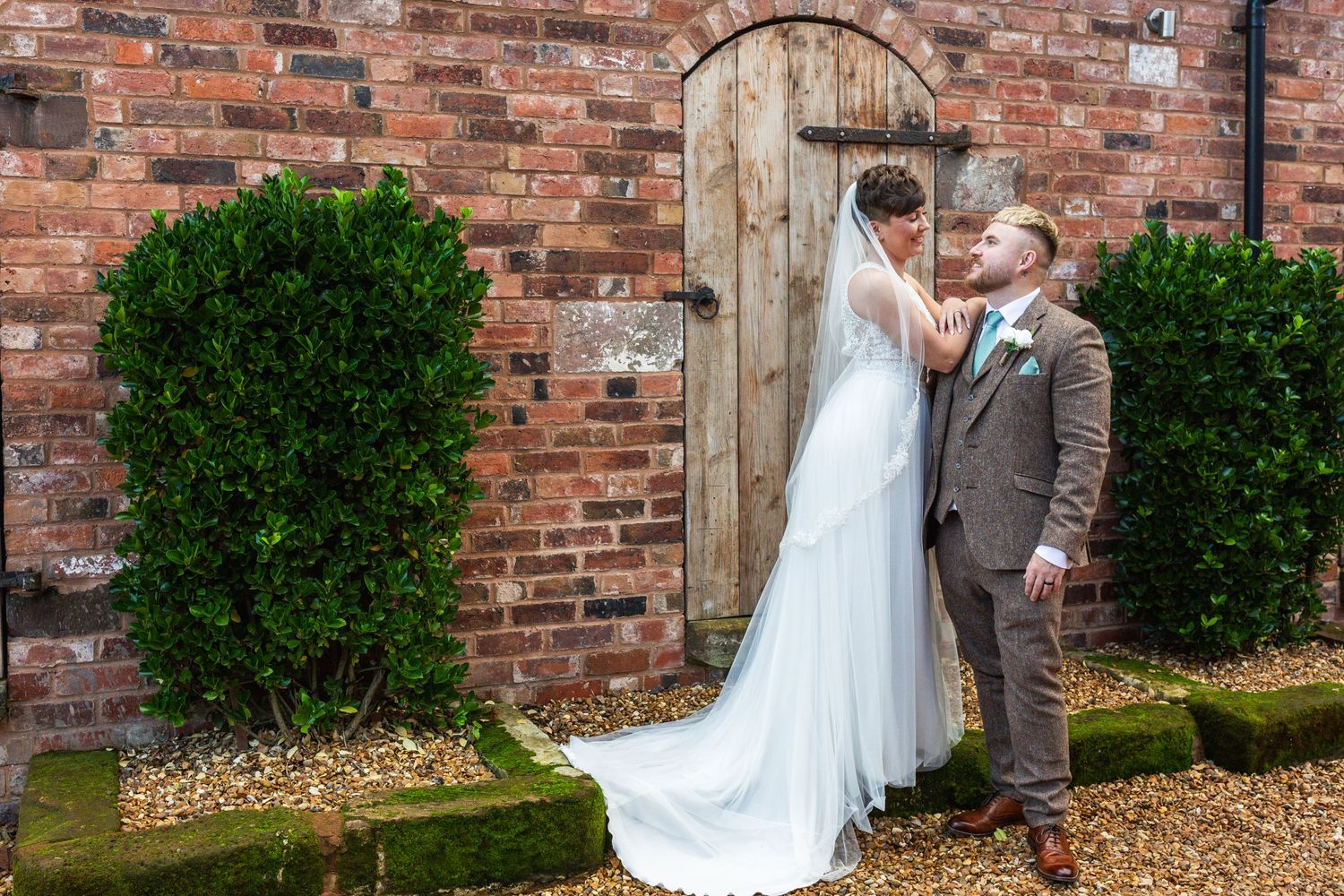 A brick wall garden setting with a rustic wooden door and manicured bushes.