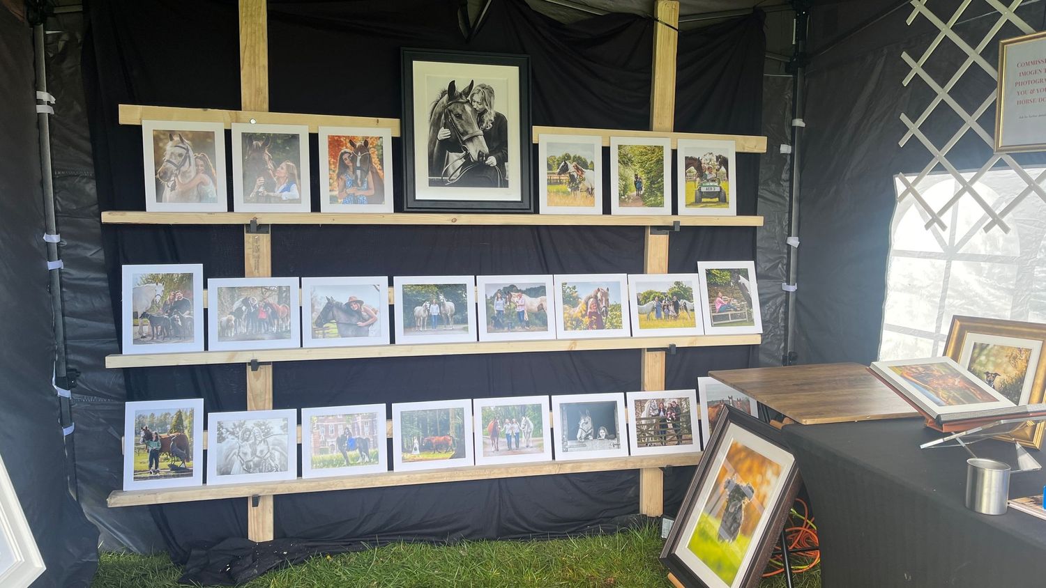 A display of vintage photographs and artwork arranged on wooden shelves against a dark backdrop in an outdoor setting.