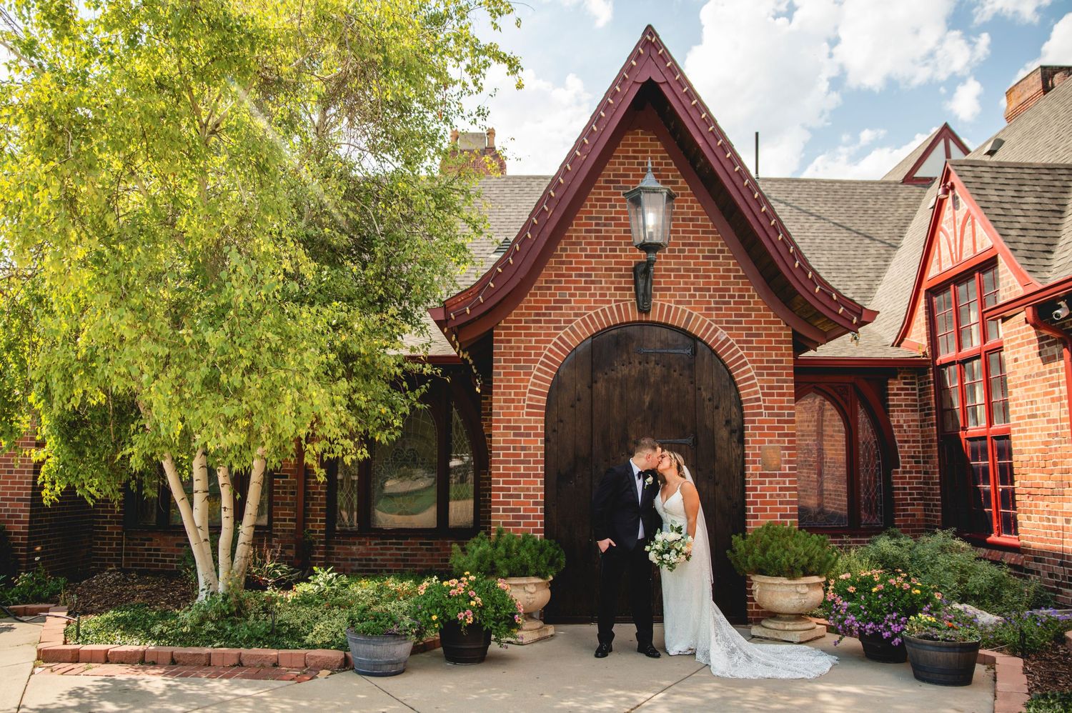 A couple stands in front of a charming brick chapel with gothic architecture and landscaped gardens.