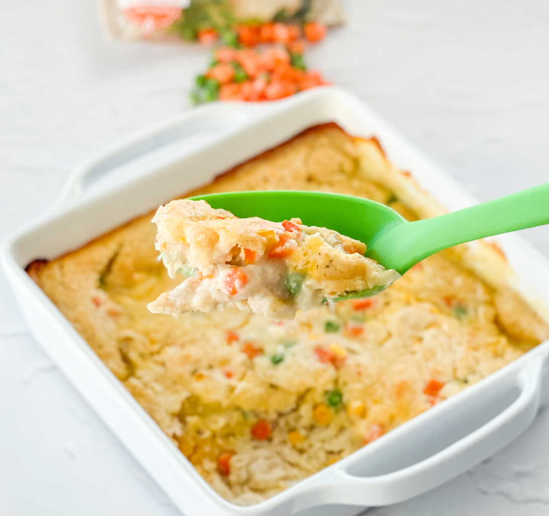 Creamy casserole dish with chunks of meat and vegetables being scooped with a green spoon.