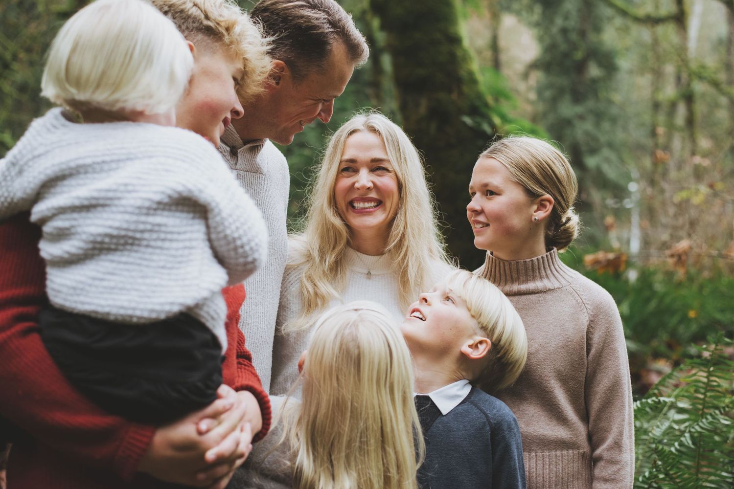 Mother beams with a broad smile while surrounded by husband and children in the woods.