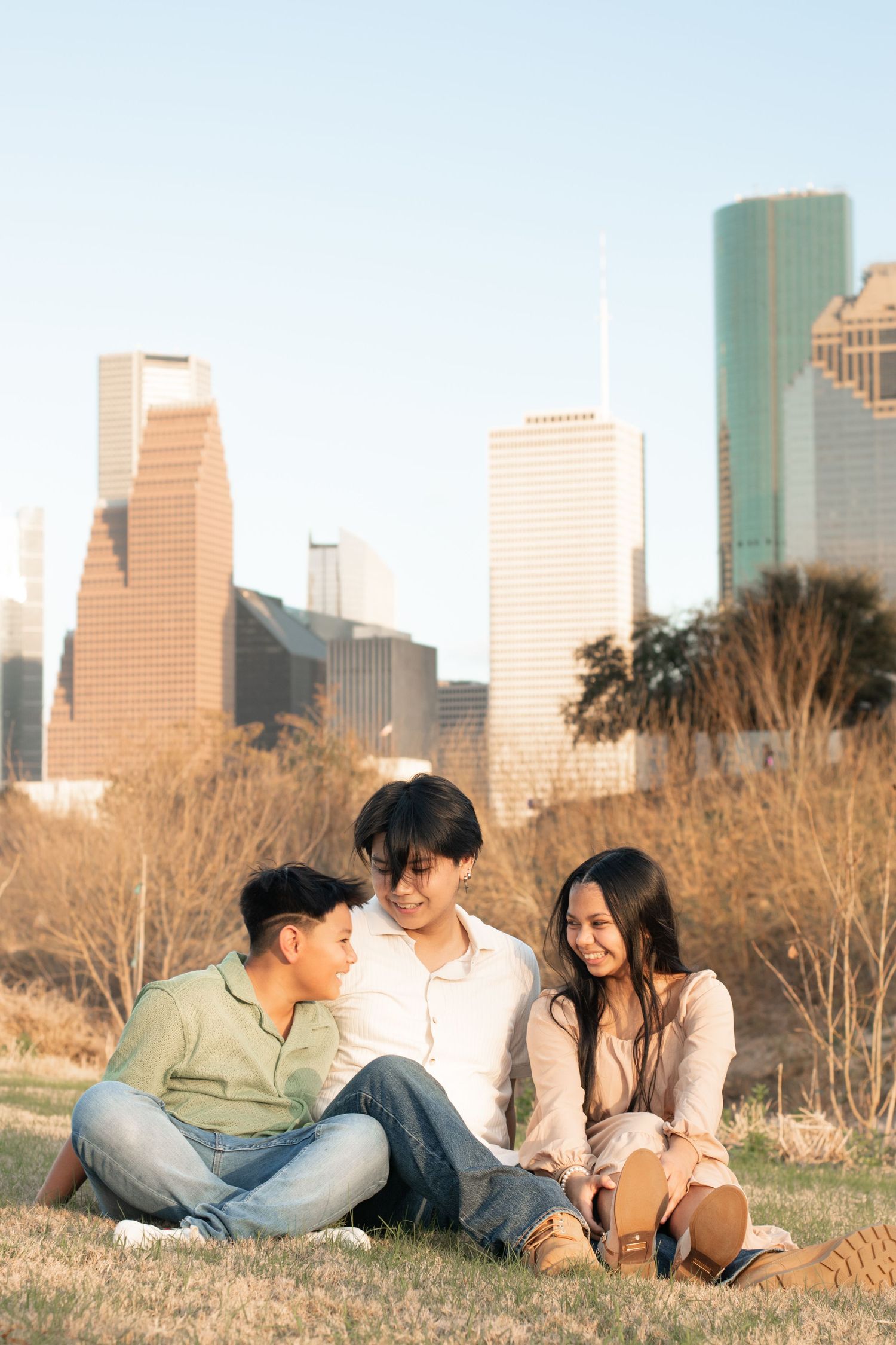 Three young people relaxing on grass hill overlooking downtown Houston skyline.