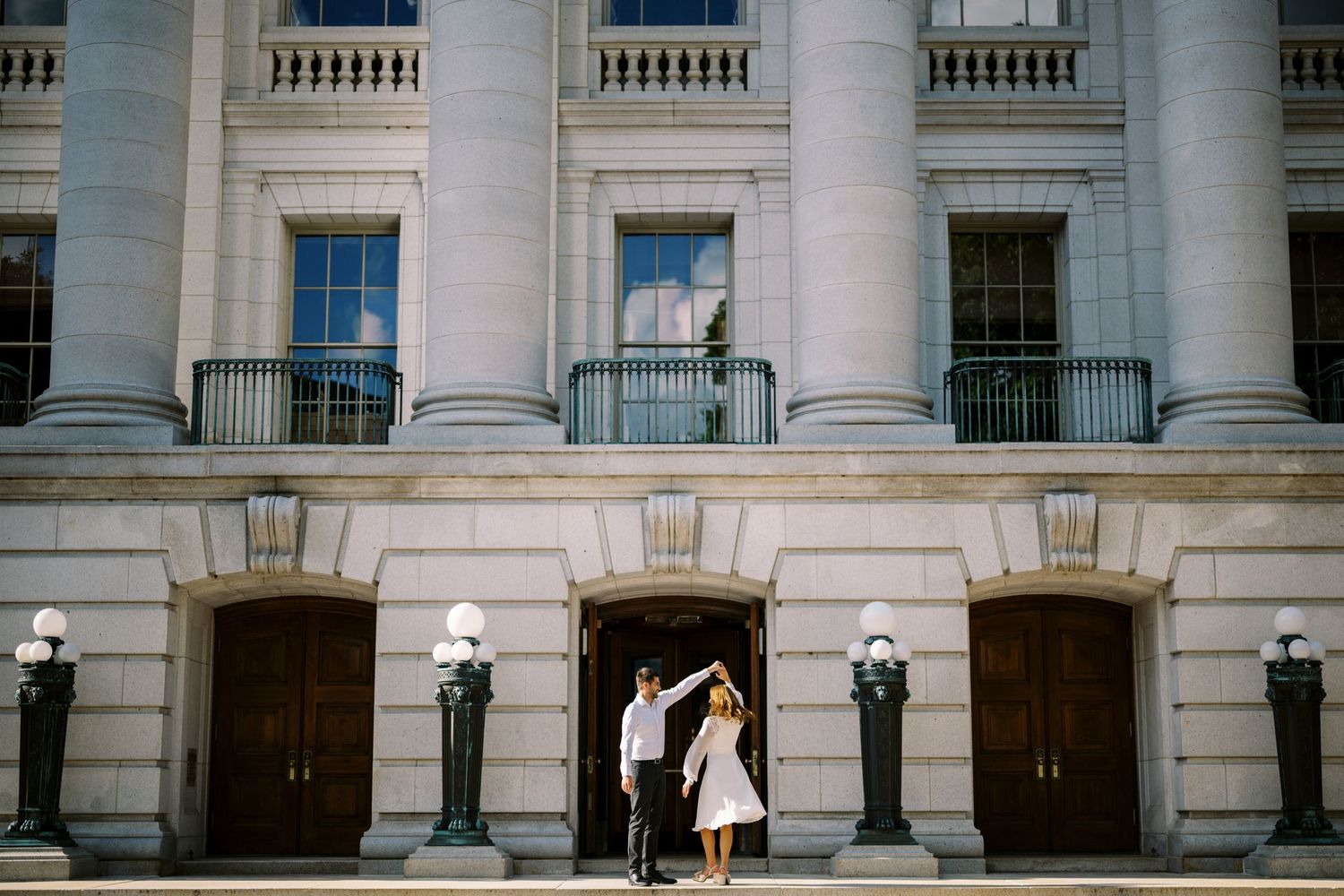 Dancing couple surrounded by elegant white pillars and grand wooden doors of a historic government building.