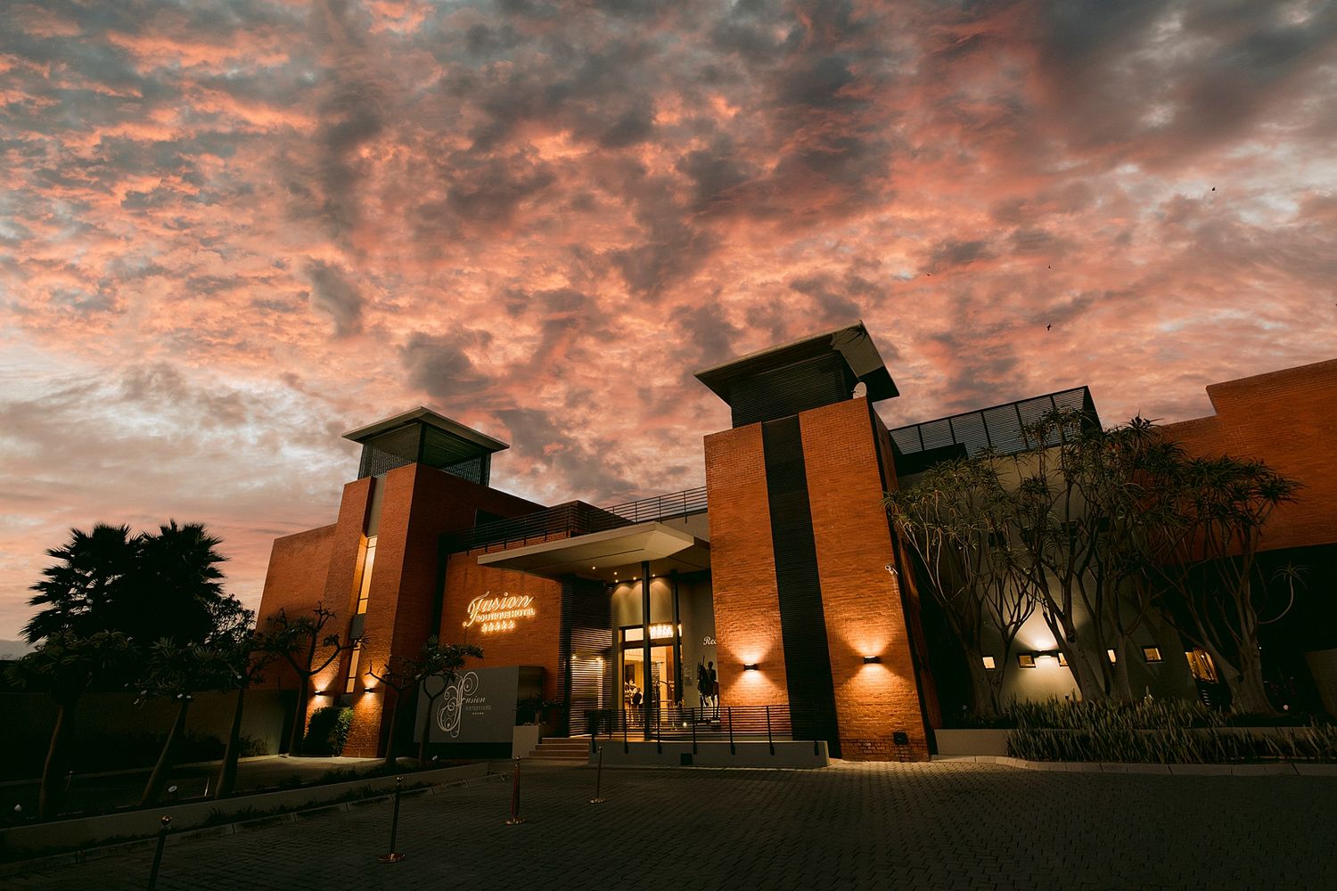 Modern building exterior glowing warmly at dusk under dramatic pink and purple sunset clouds.
