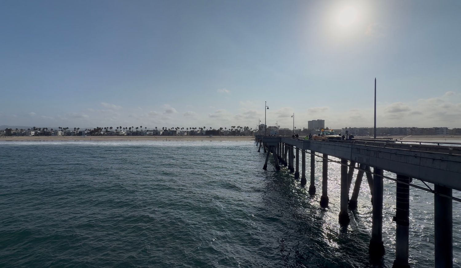 Scenic ocean pier extending into calm blue waters under a bright sunny sky with coastal cityscape in the background.