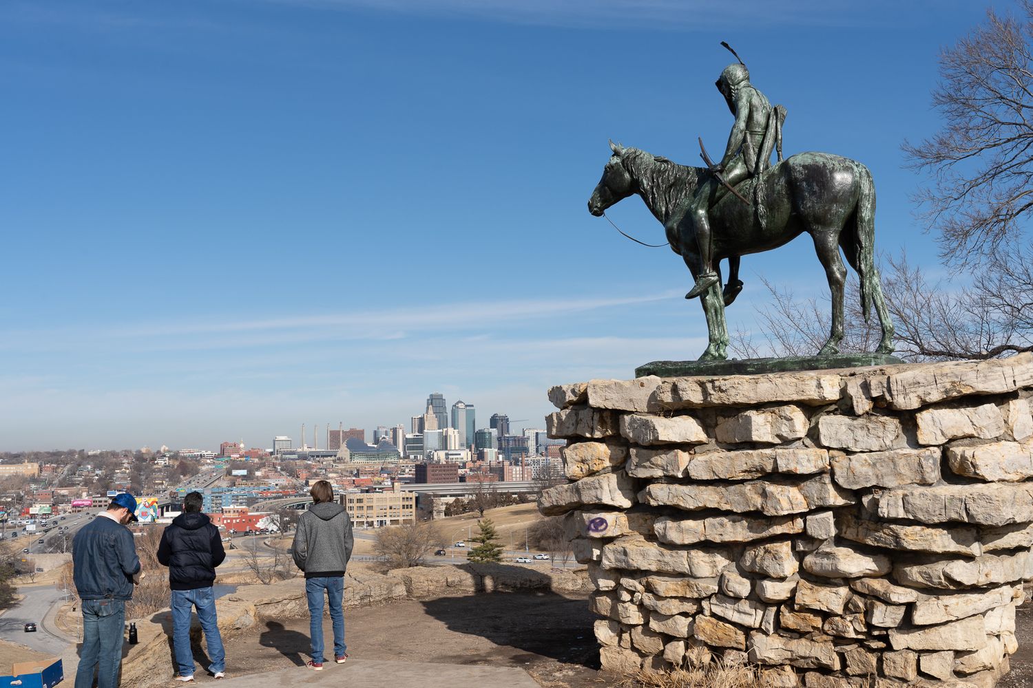 A bronze horse statue overlooks the Kansas City skyline from a stone wall at Scout's Lookout observation point.