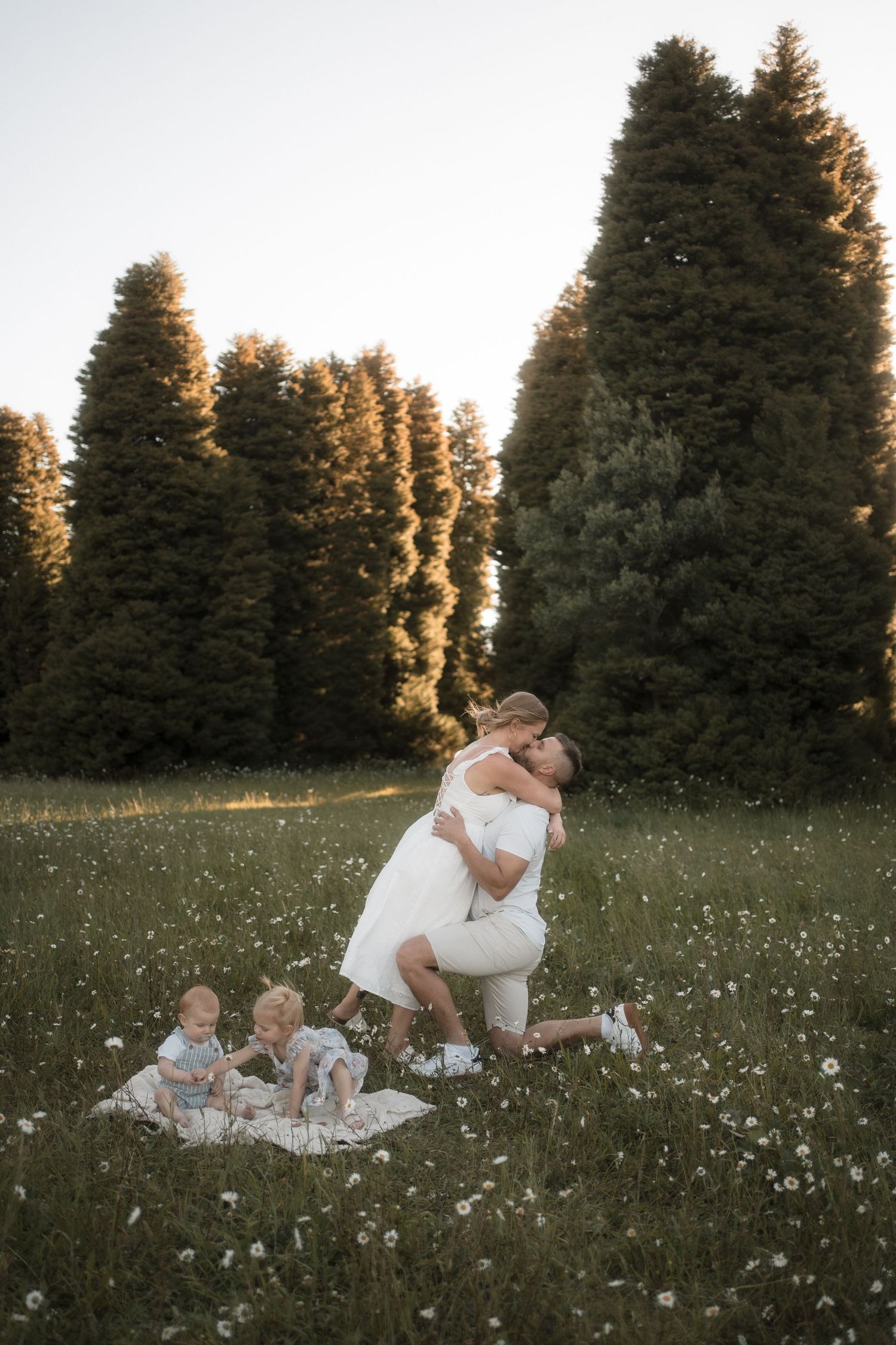 Family enjoying a peaceful summer evening together on a blanket in a wildflower meadow at sunset.