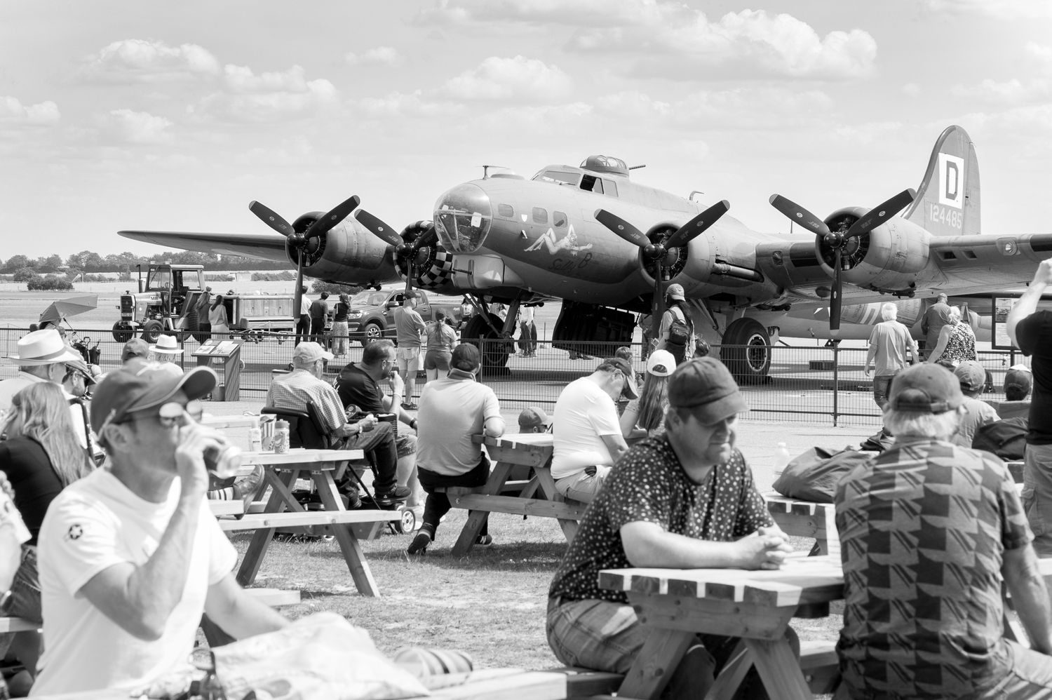 Crowd gathered at an airshow with a vintage WWII B-17 Flying Fortress bomber on display at a sunny airfield.