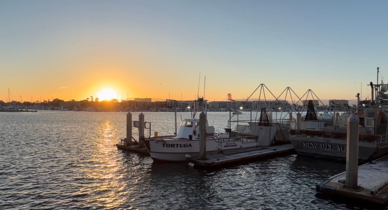 Fishing boats docked at a harbor pier during a golden sunset over calm water.