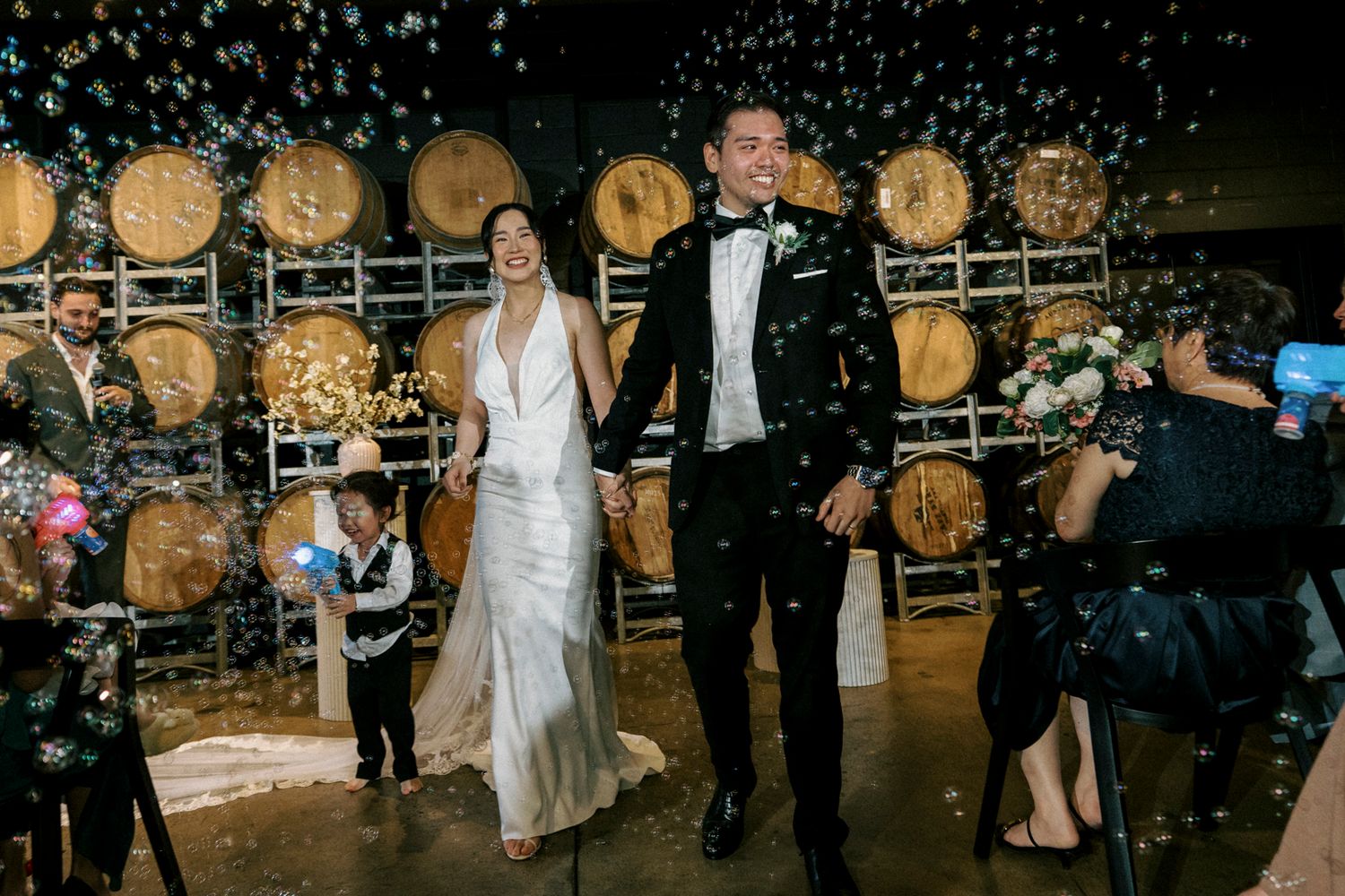 Bride and groom walk through confetti shower in winery wedding venue with wooden barrels backdrop at the bethnal. Newstead Brisbane
