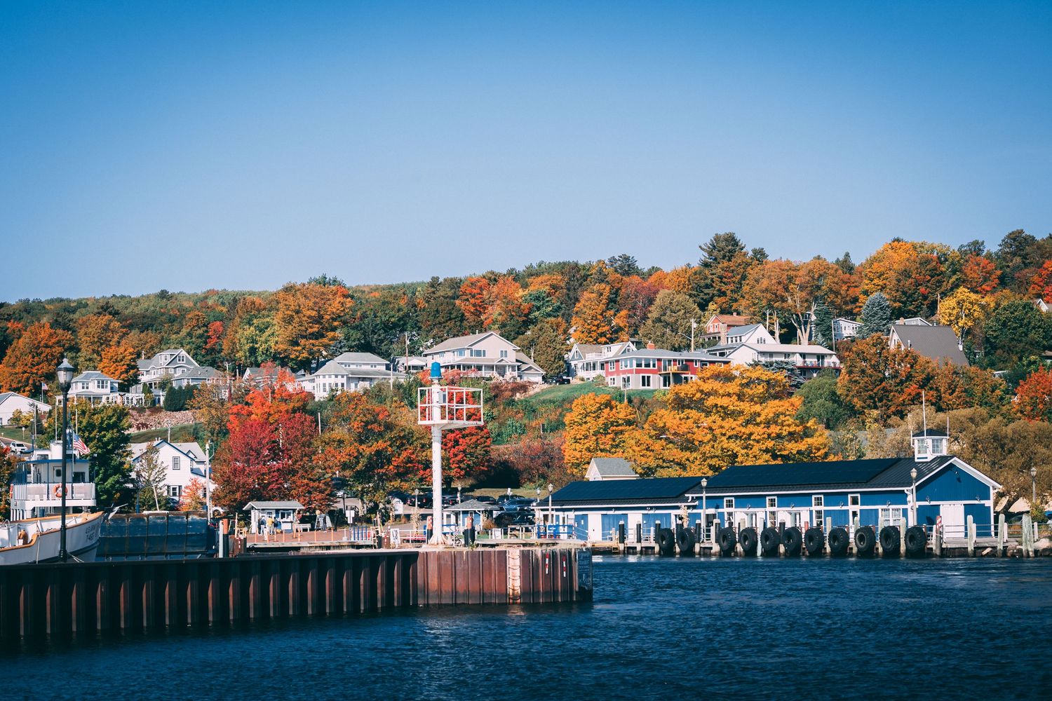 Bayfield Wis. Colorful autumn foliage frames a charming waterfront town with houses and a blue dock under a clear sky.