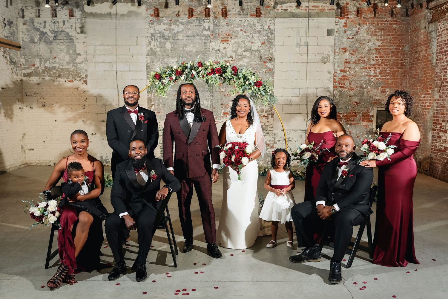 Baltimore Wedding party members in burgundy and black attire pose together against a rustic stone wall background.