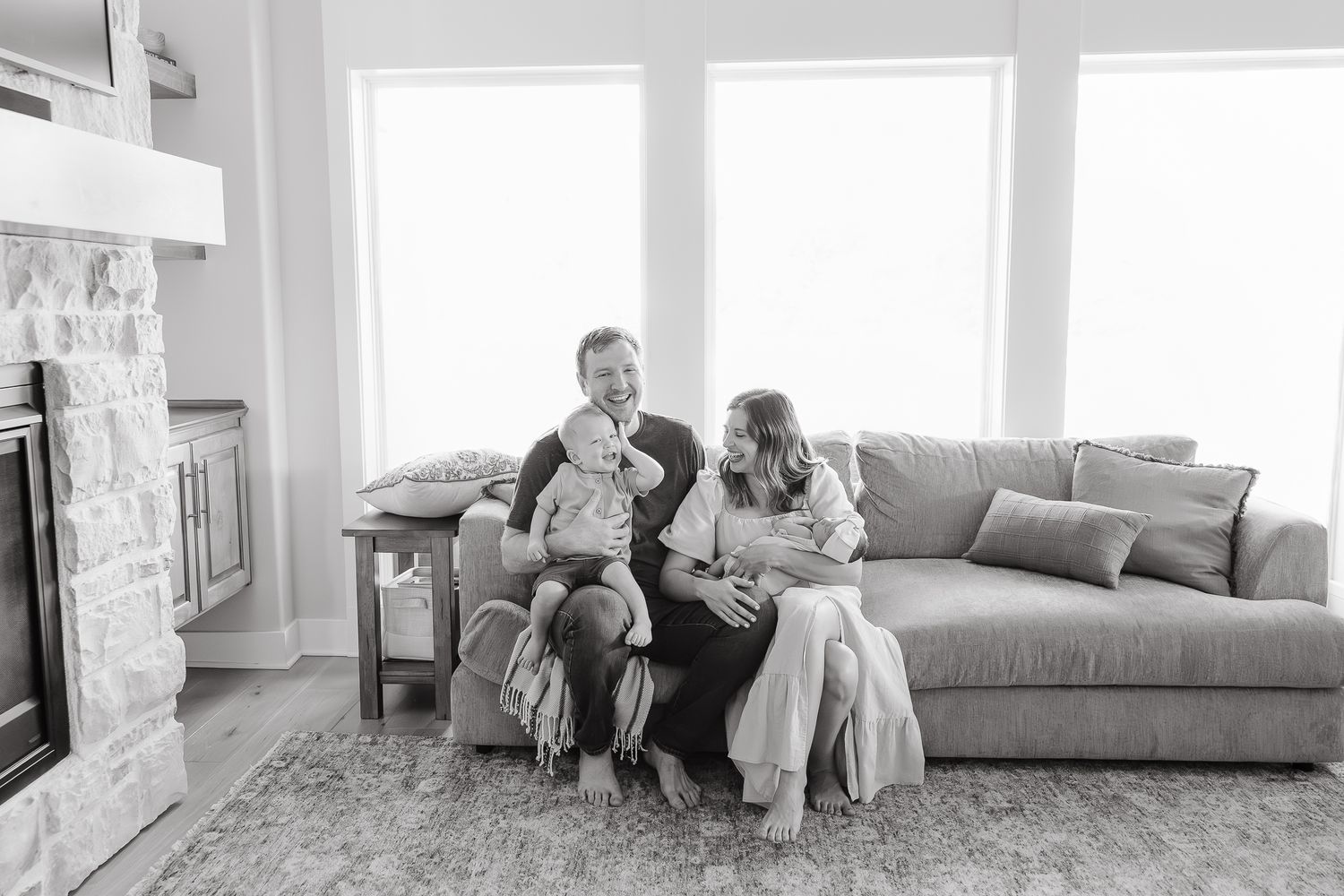 family sitting on couch in living room smiling snuggling together kansas city newborn photography session