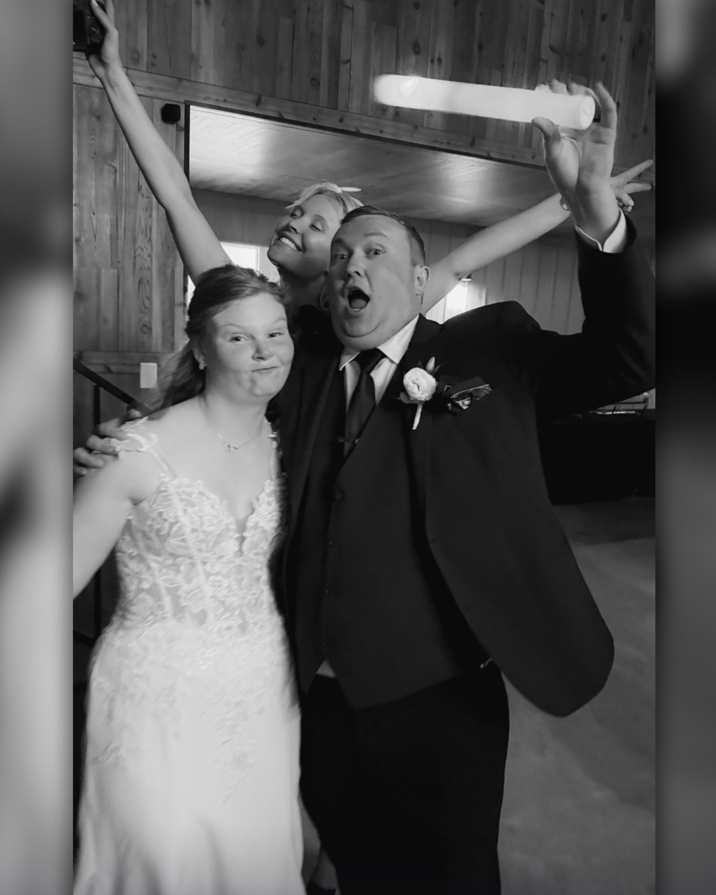 Black and white photo of a bride and groom celebrating joyfully with a friend at their wedding reception.