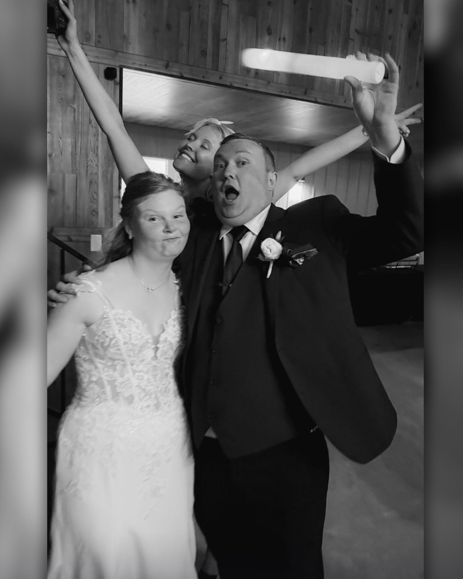 Black and white photo of a bride and groom celebrating joyfully with a friend at their wedding reception.
