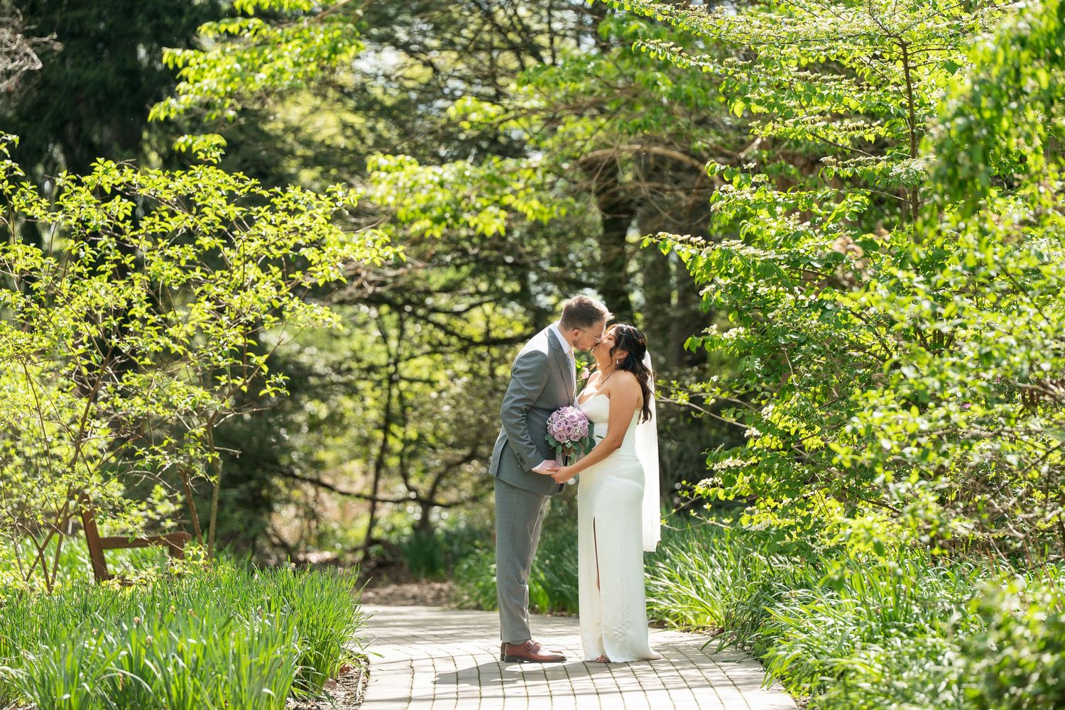 Bride and groom sharing a romantic moment on a garden pathway surrounded by lush spring greenery.