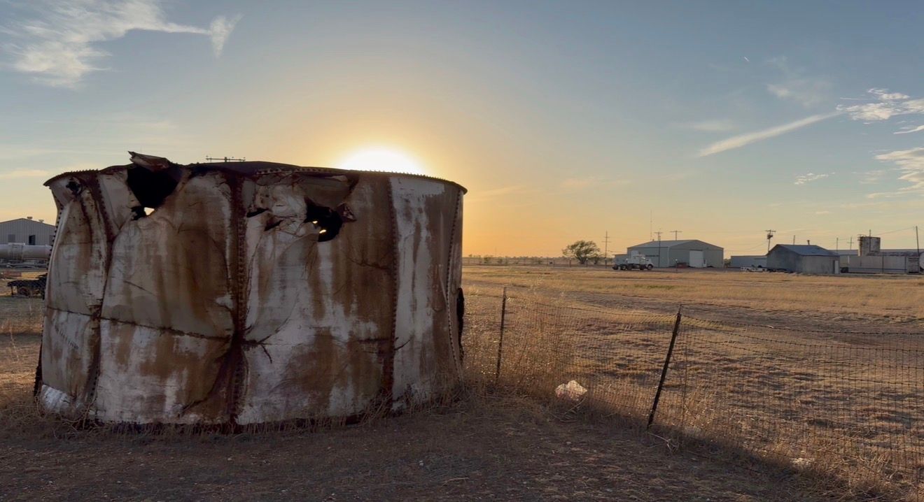 Rusty abandoned grain silo at sunset on a dry rural farm landscape with open sky.