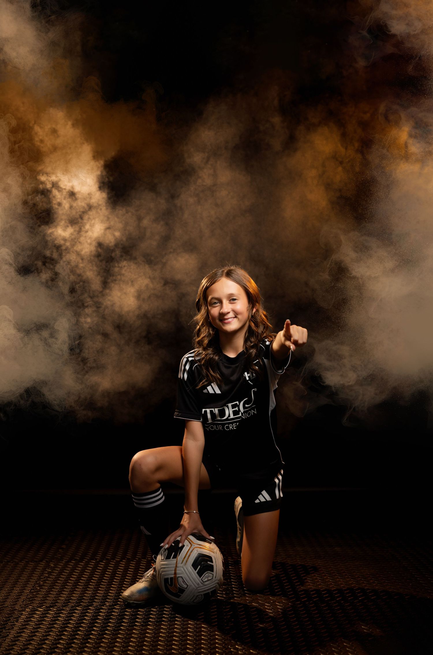 Dramatic sports portrait of a soccer player with colored fog, a dark backdrop, and dramatic lighting in the background