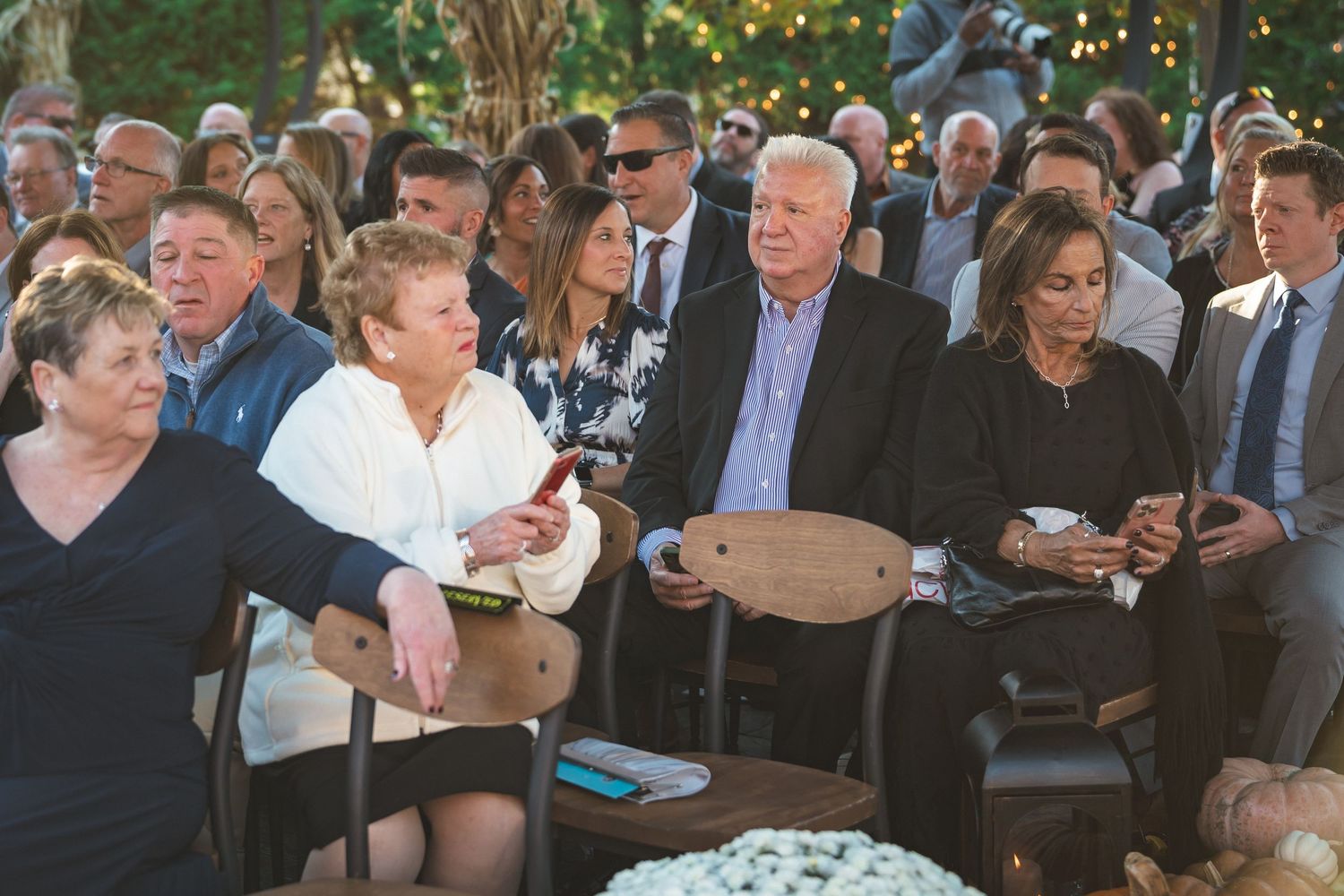 Guests seated outdoors with phones and cameras out before an unplugged wedding ceremony request