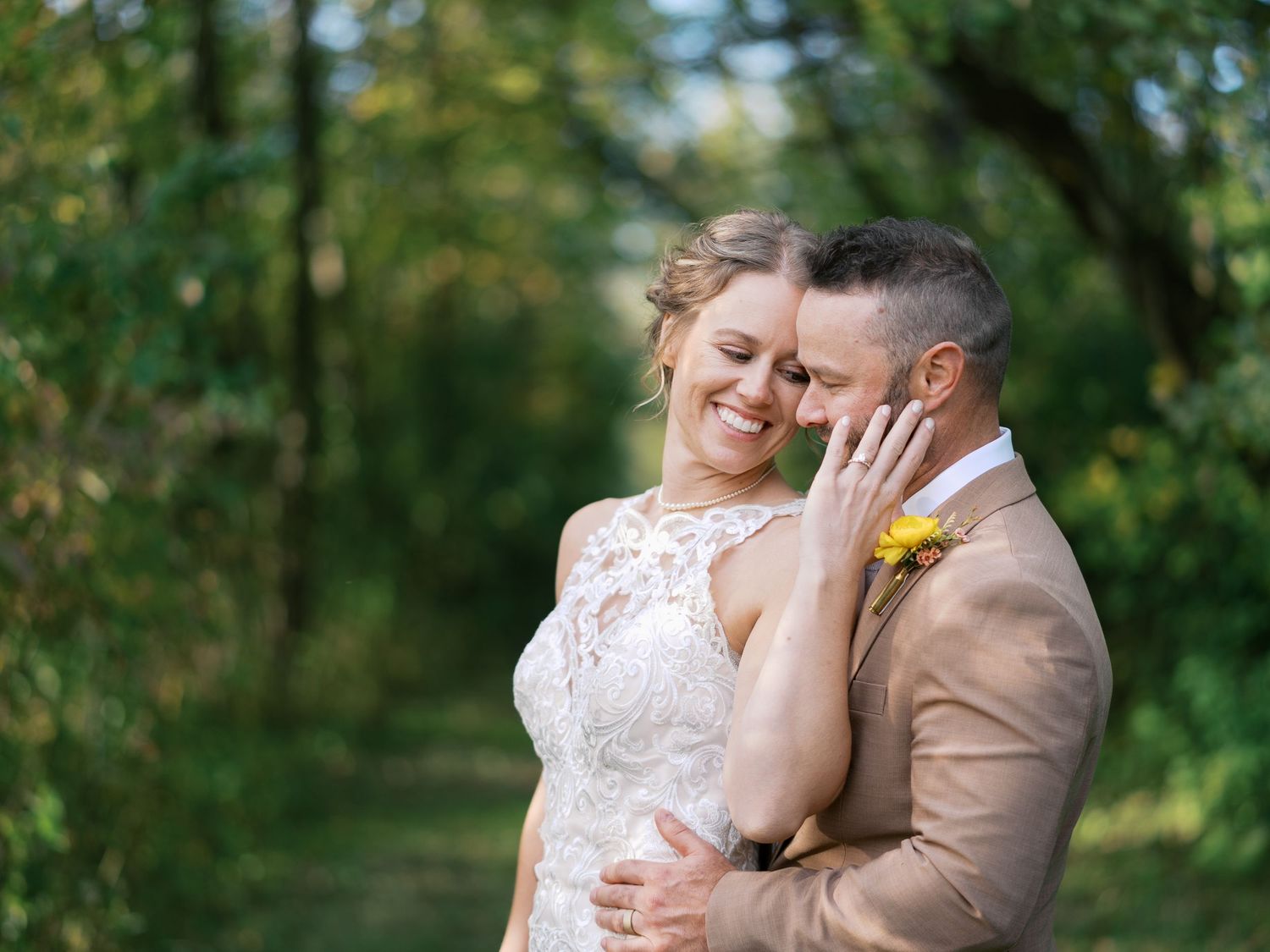 A wedding couple poses together outdoors, with the bride in a lace gown and groom wearing a yellow tie.