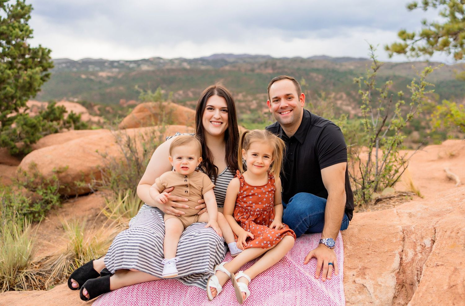 A family of four poses together on red rock formations in the garden of the gods