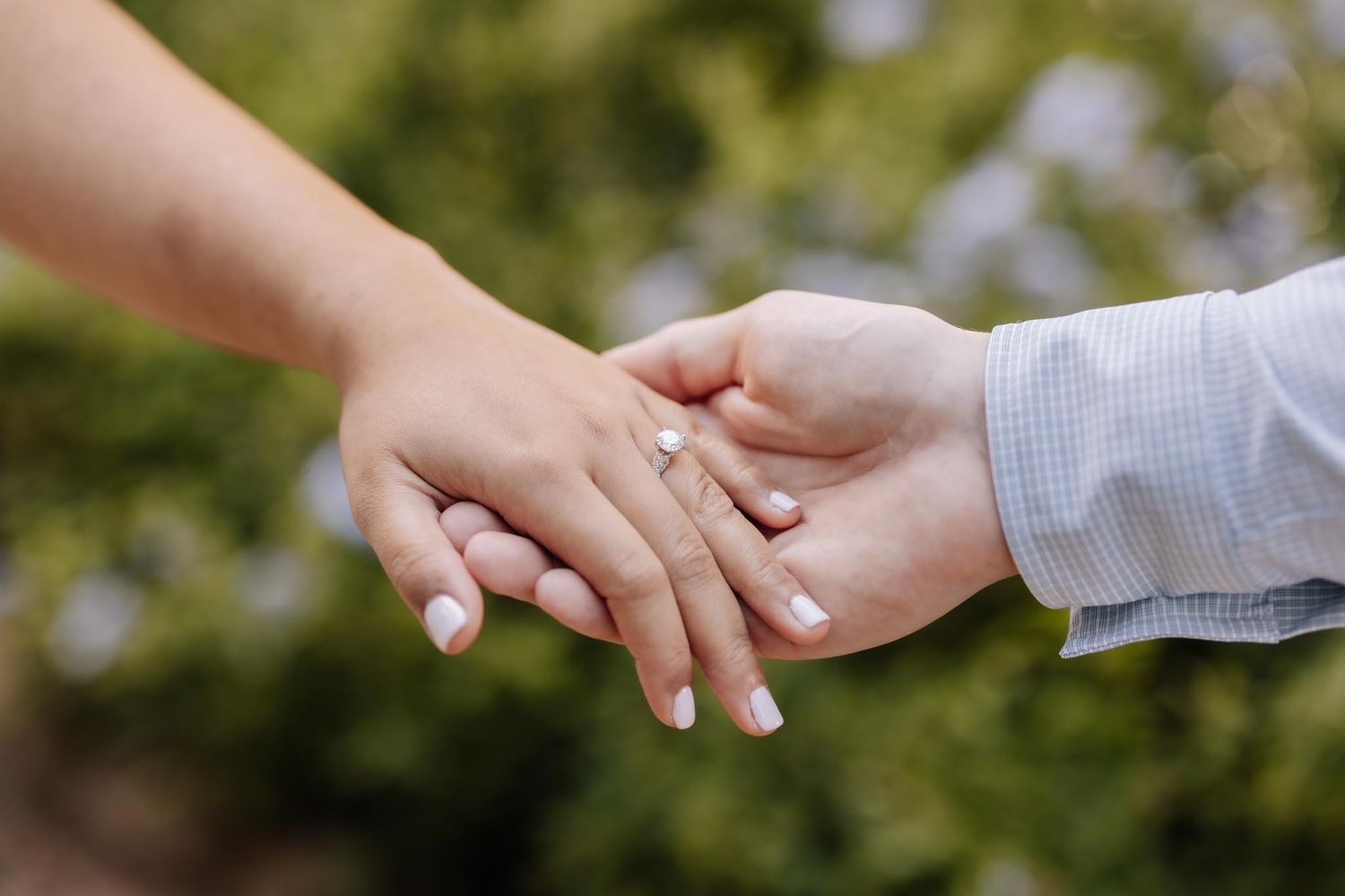 A romantic couple shares tender moments in a garden filled with white wildflowers on a sunny afternoon.