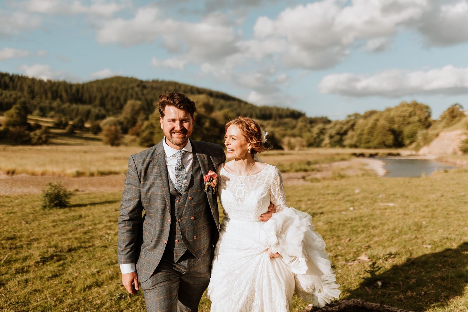 A happy couple embraces in a golden meadow with mountain views and dramatic clouds on their wedding day.
