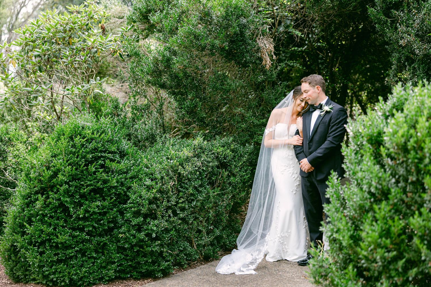 A romantic Raspberry Plain Manor wedding couple embraces in a lush garden setting surrounded by verdant greenery on their special day.