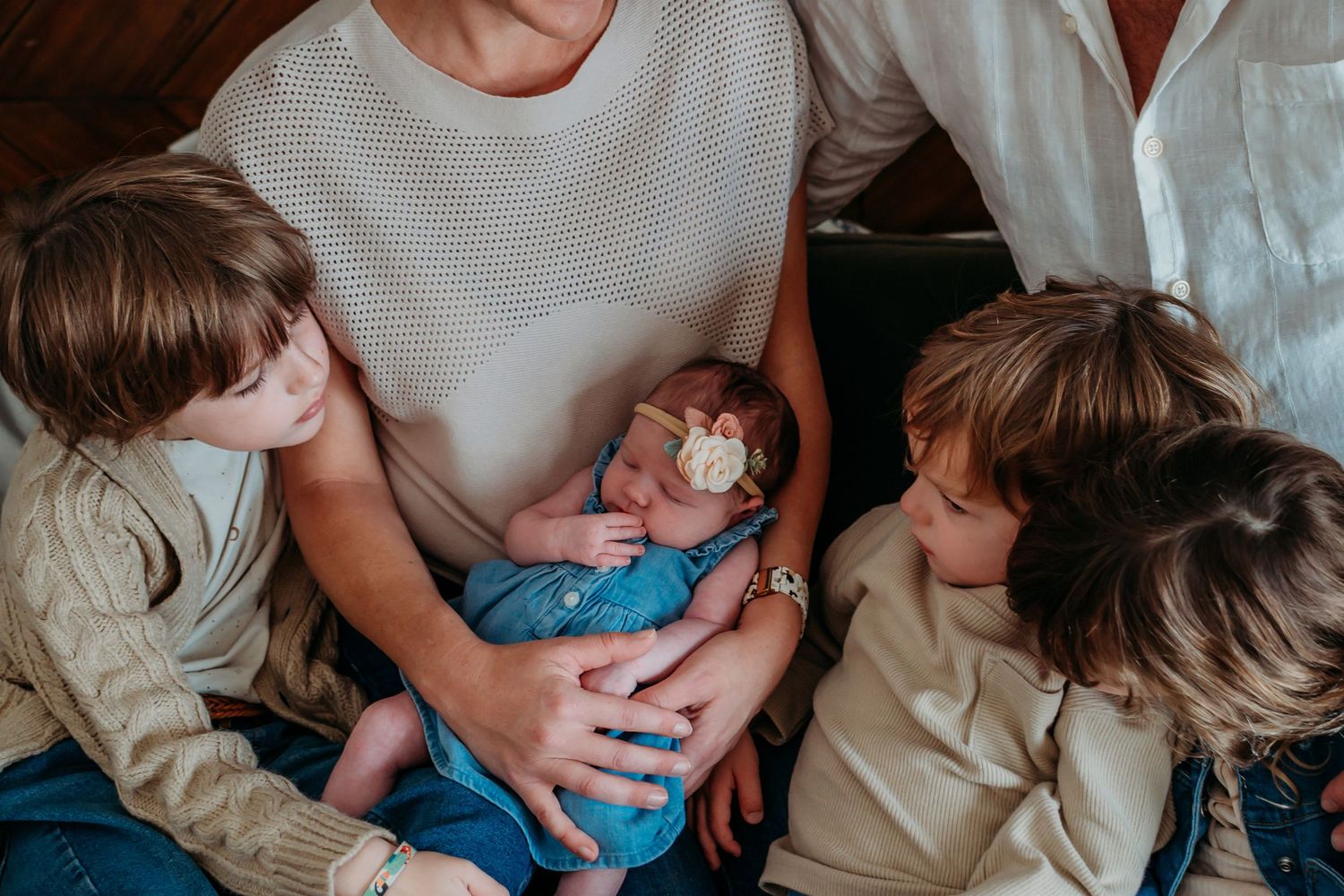 A mother holds her newborn baby in a blue outfit while two older siblings lean in adoringly during a family photo session.