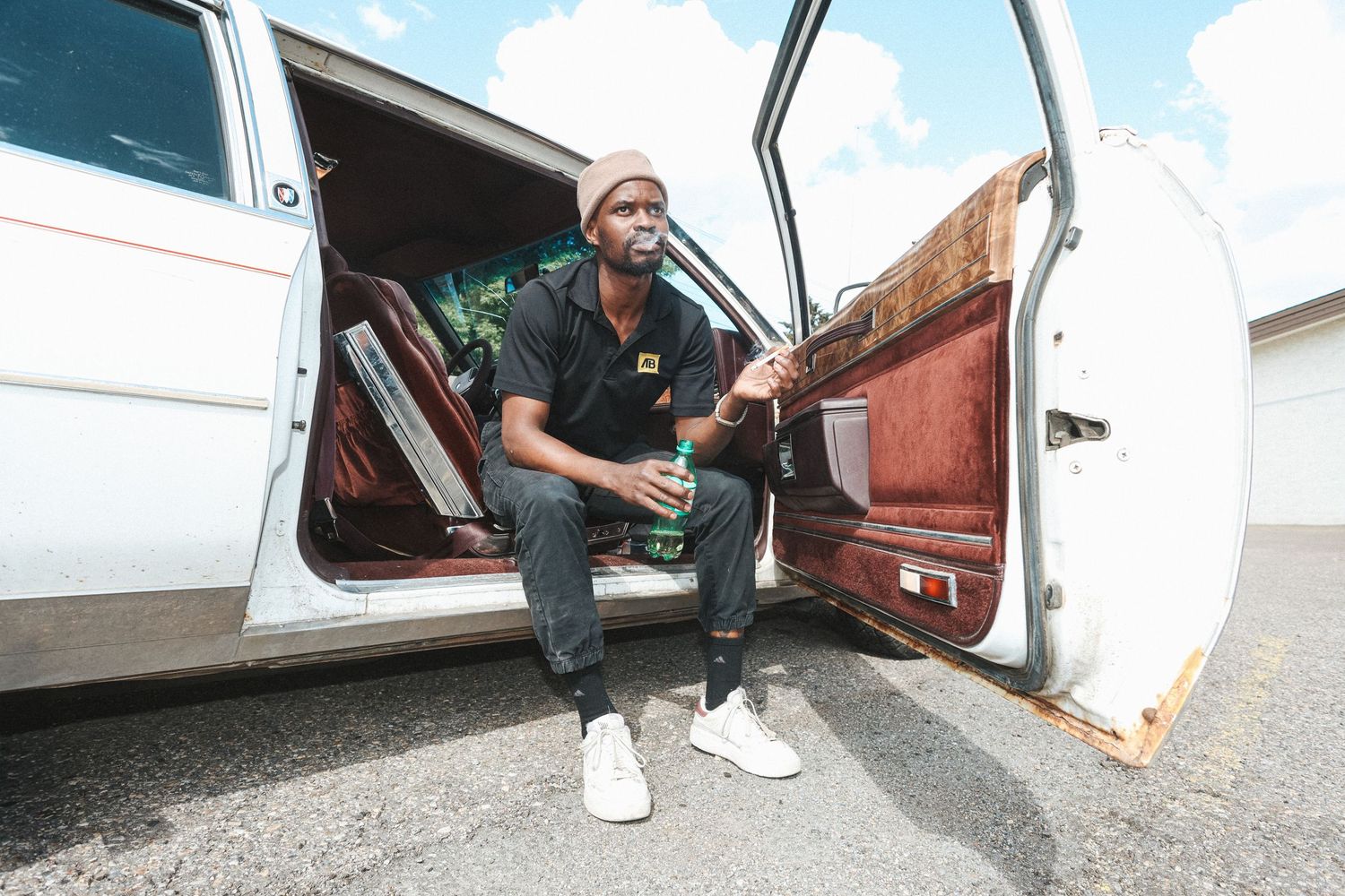 Man sitting in an open car door holding a drink, styled portrait for editorial vs fashion photography blog