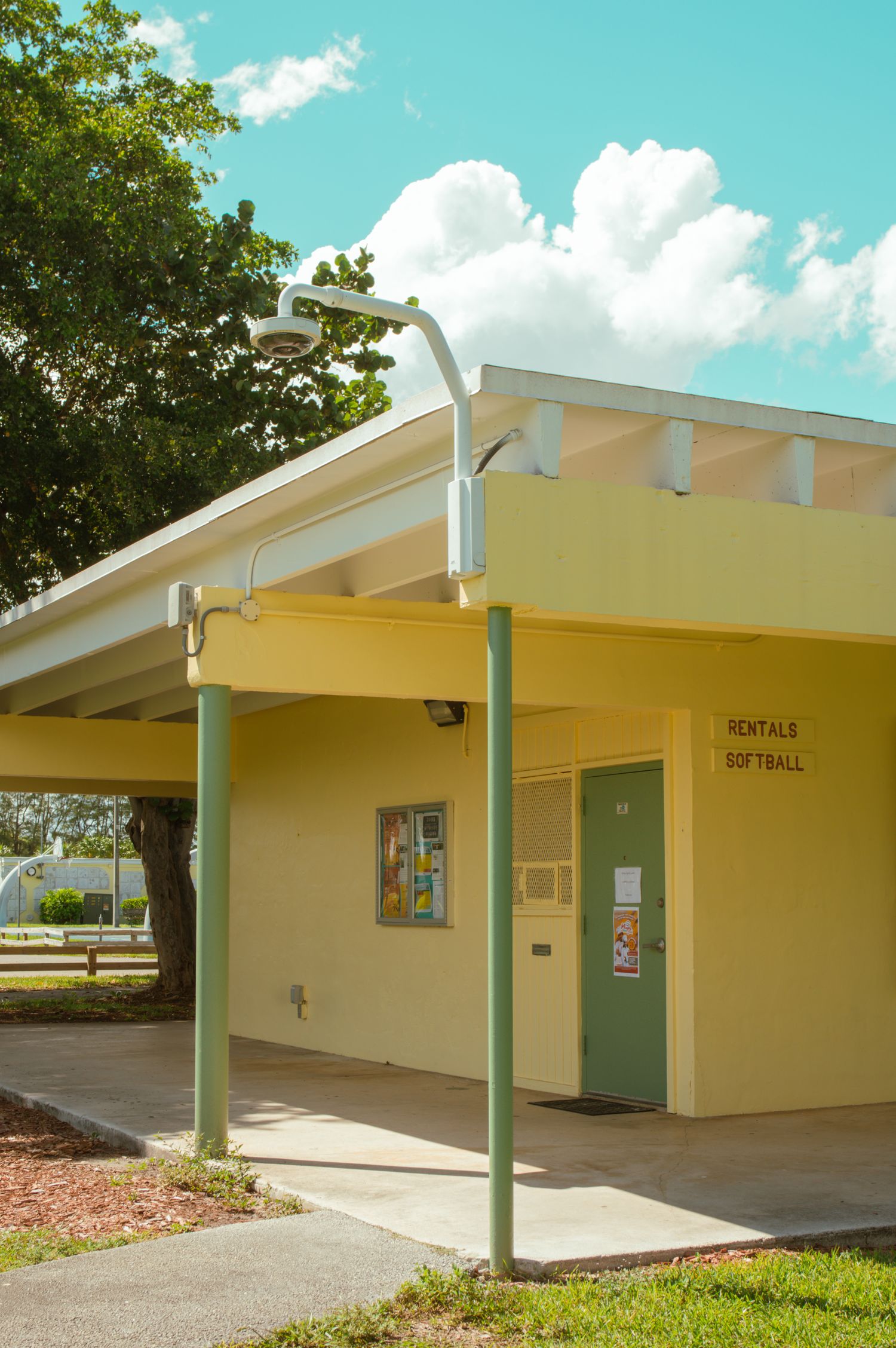 Yellow public restroom building with white trim and covered walkway at a park under bright blue sky.