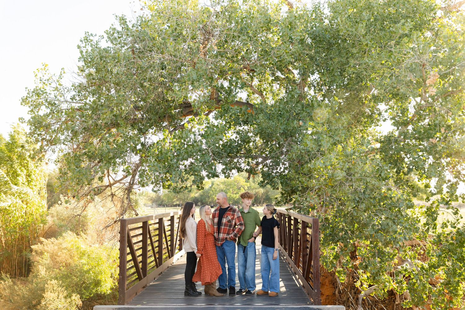 Kirkland fields a stunning large tree with a family of 5 standing on a bridge looking at each other in beautiful st. george utah