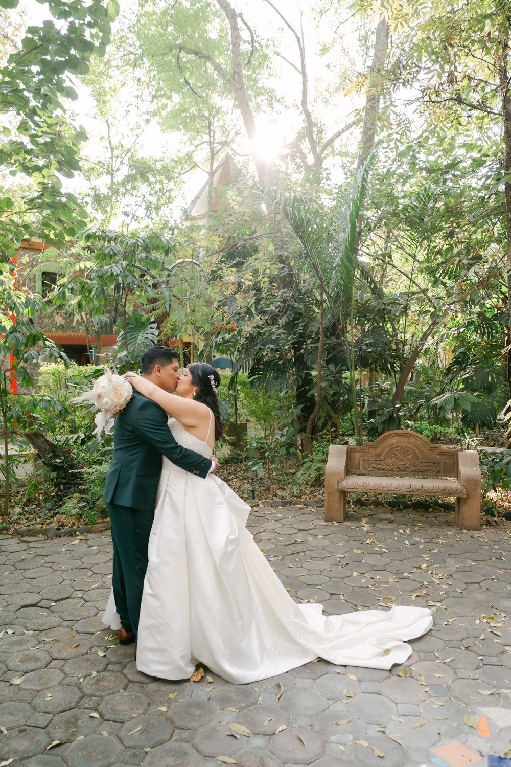 At Casa de los Arboles, a couple shares a romantic dance moment on a stone patio surrounded by lush garden greenery and sunlit trees.