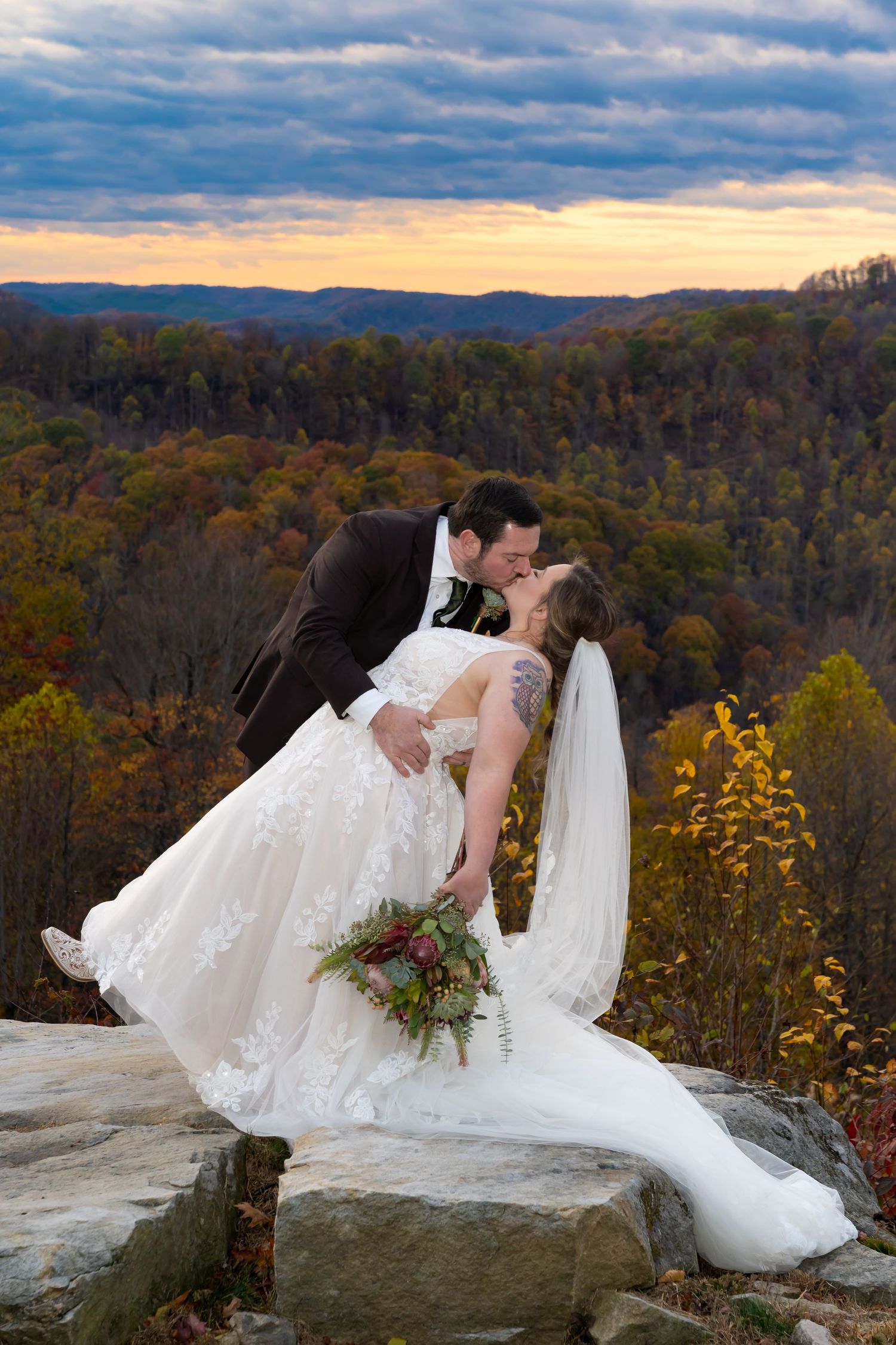 A couple in wedding attire dances together in a misty wooded outdoor setting during their celebration.