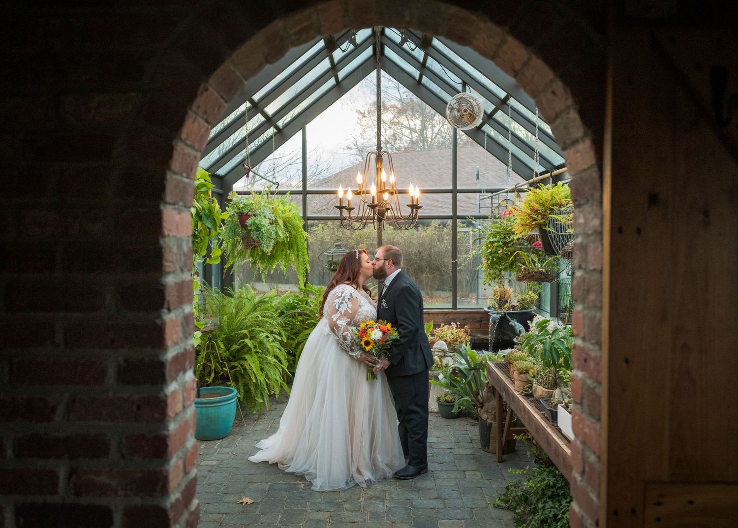 Newlyweds share an intimate moment outdoors with autumn foliage and rustic architecture in background.