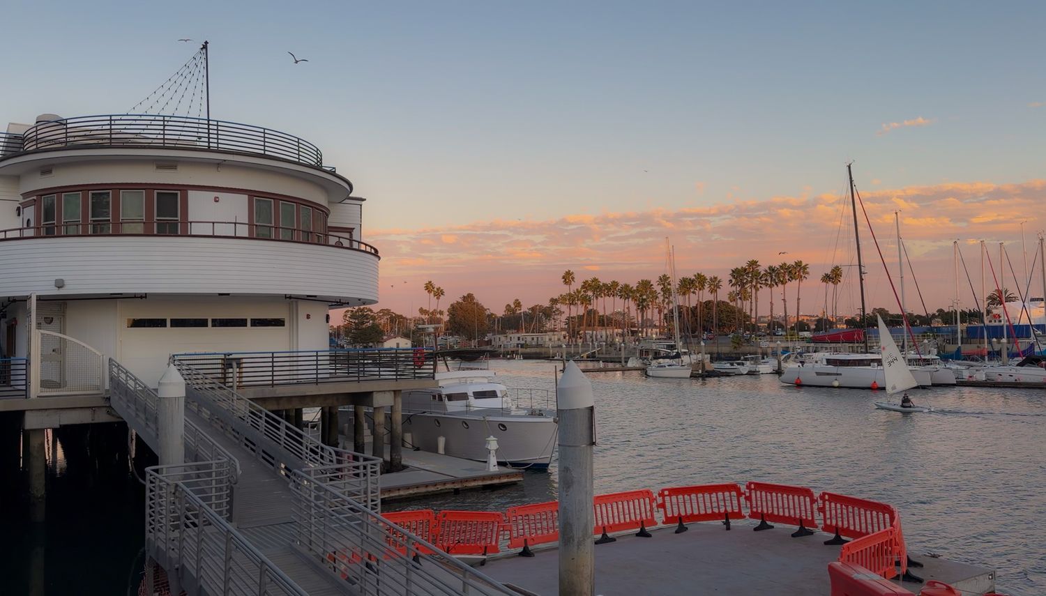 Panoramic view of a marina with boats docked at sunset showing multiple vessels and waterfront buildings.