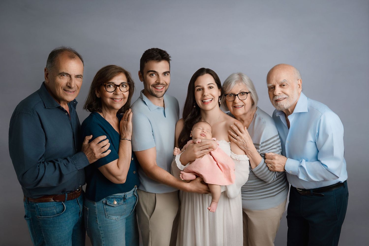 Multi-generational family in casual clothing posing together against a grey background for a studio portrait.