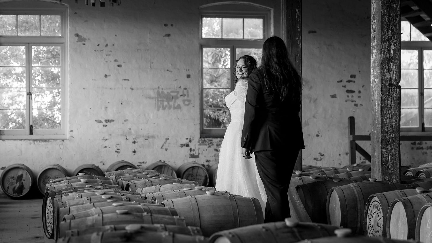 A black and white panoramic view of a Bride and Groom walking through a Winery Barrel room at the Corowa Distilling Company.