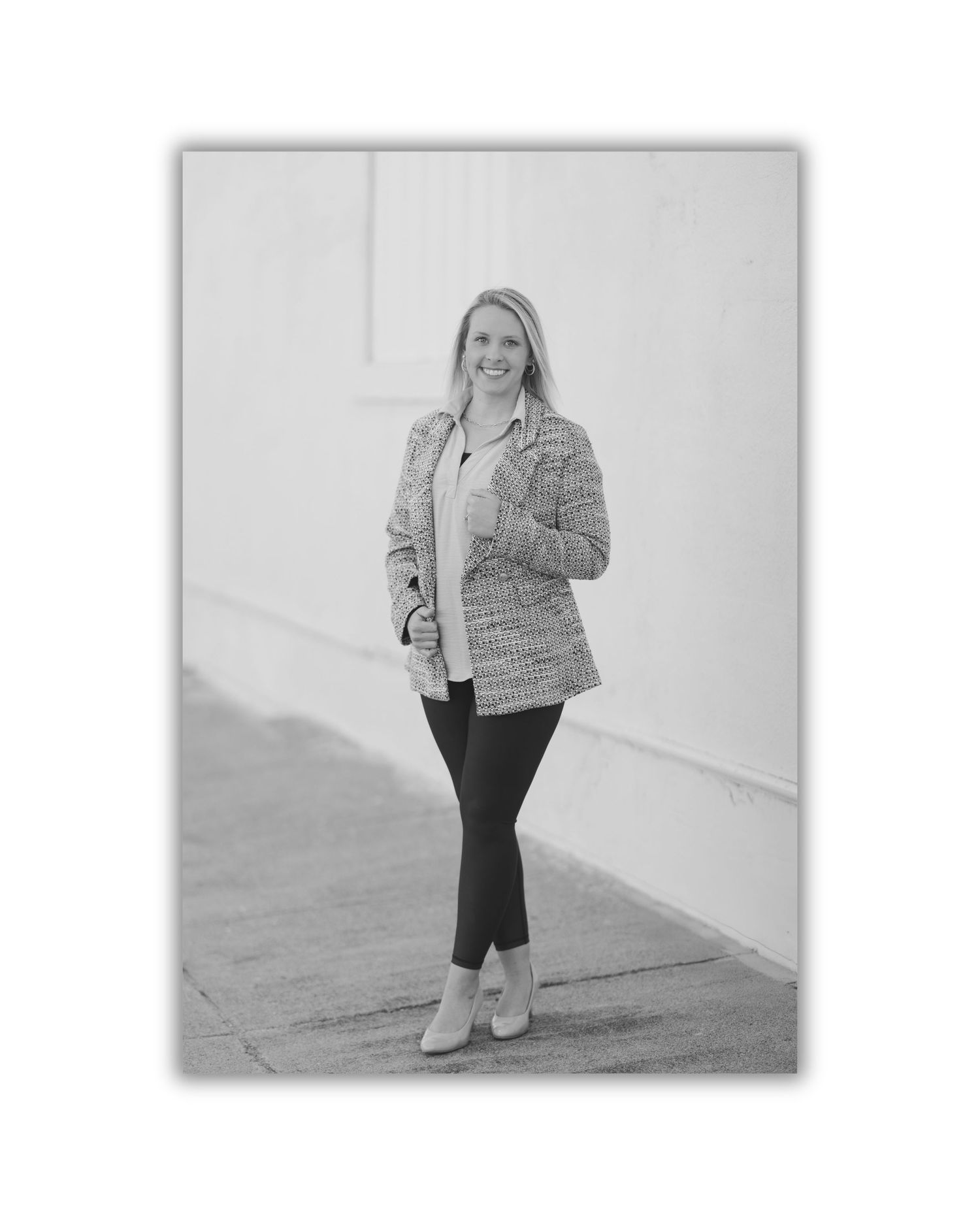 Woman wearing a quilted jacket and black pants poses casually against a white wall in an outdoor setting.