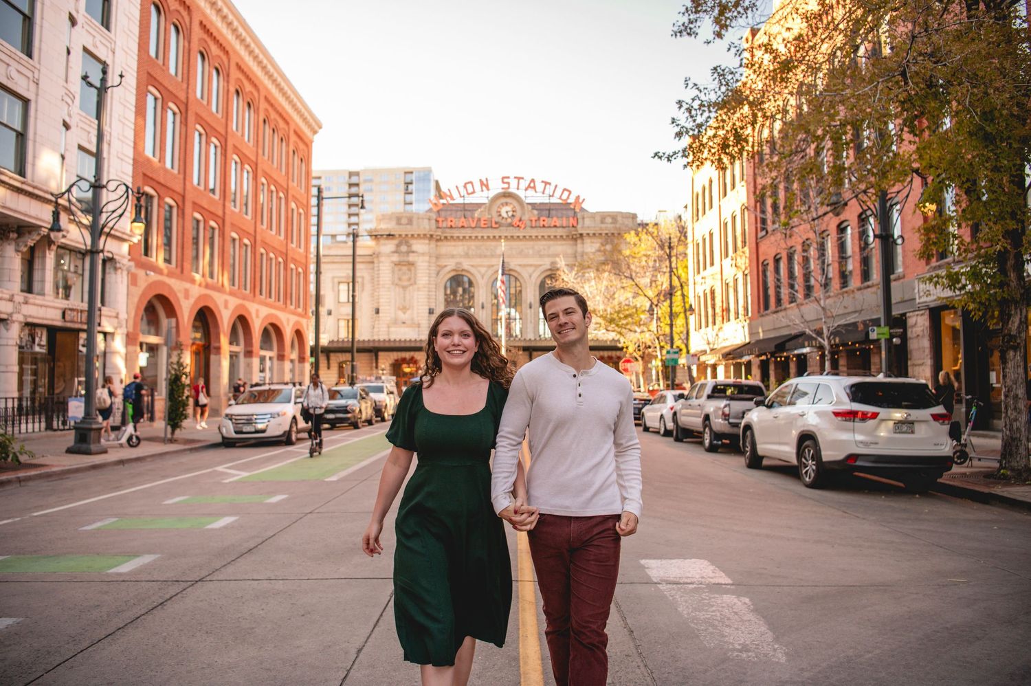 Couple smiling and holding hands on a city street near Union Station on a sunny fall day.