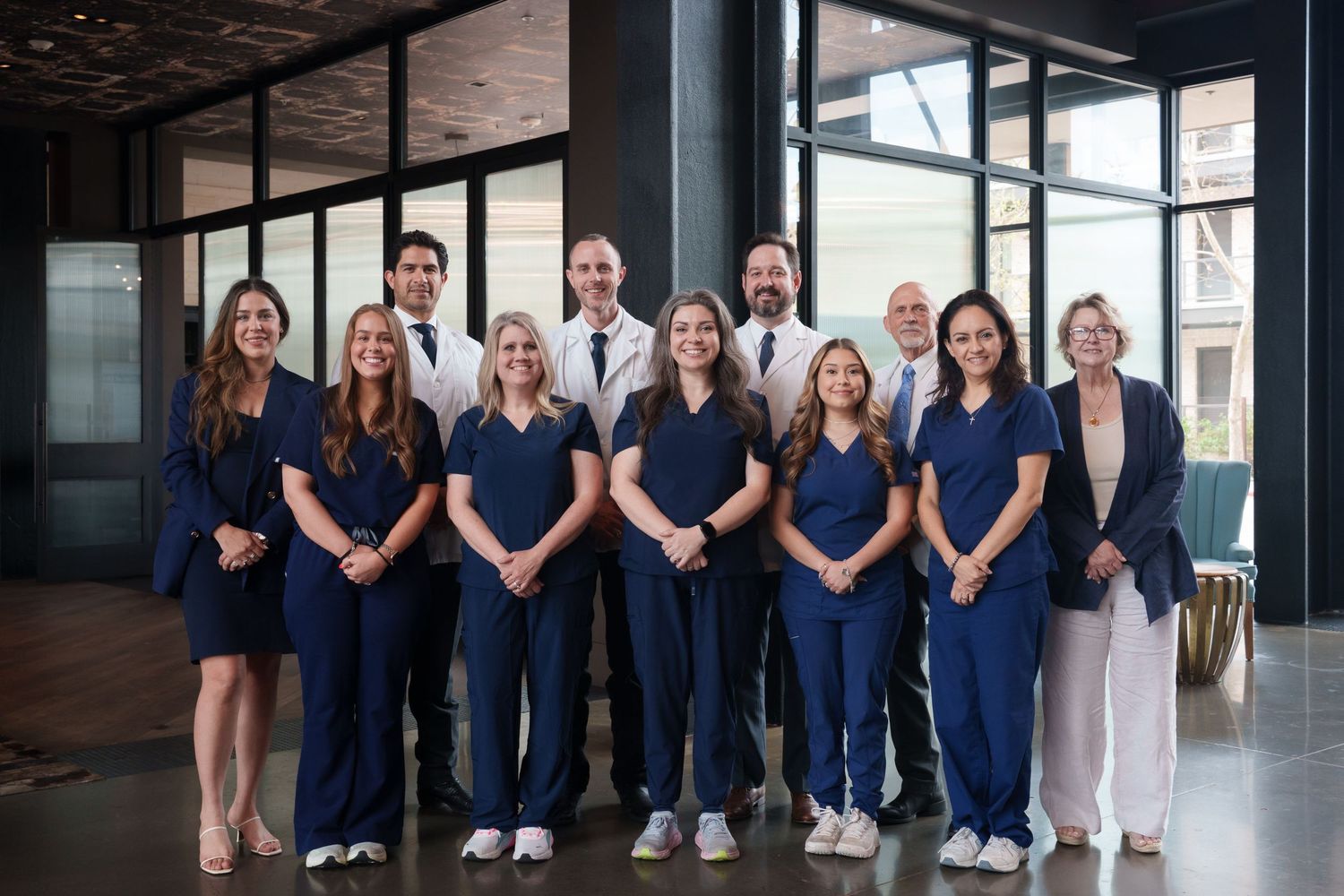 A professional medical team in navy scrubs poses for a group photo in a modern building lobby.