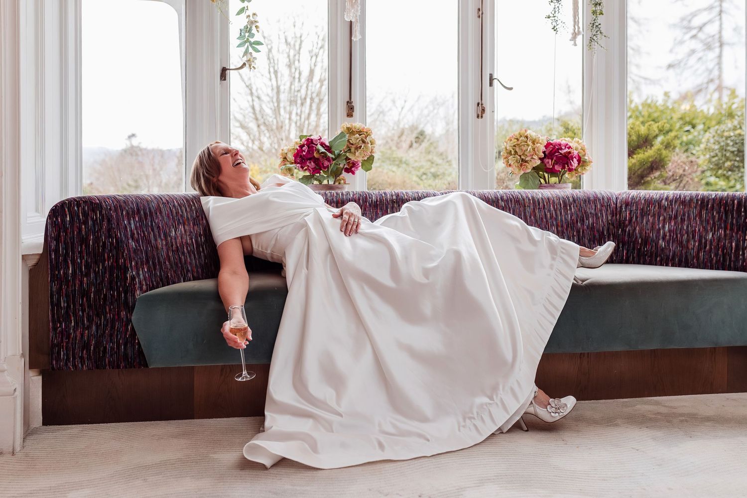 Bride laughing in wedding dress holding a glass of wine during relaxed Lake District wedding