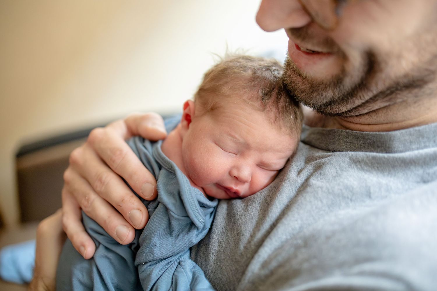 Loving father gently holds sleeping newborn baby against his chest in a tender embrace.