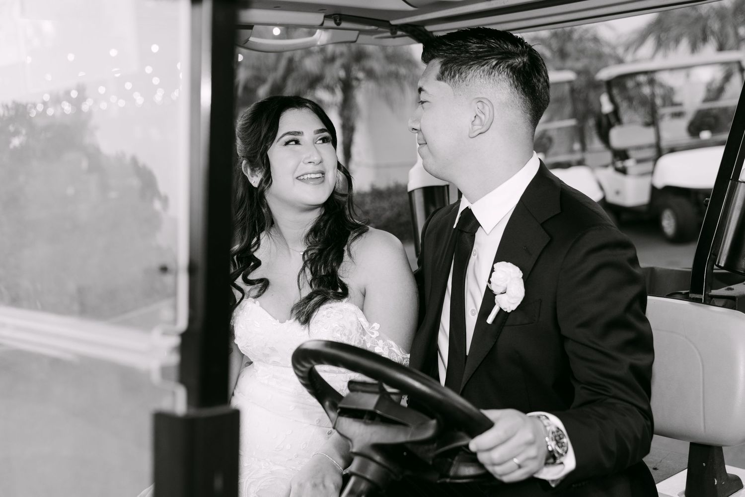 Black and white photo of a bride and groom sitting in a vintage vehicle, smiling joyfully on their wedding day.
