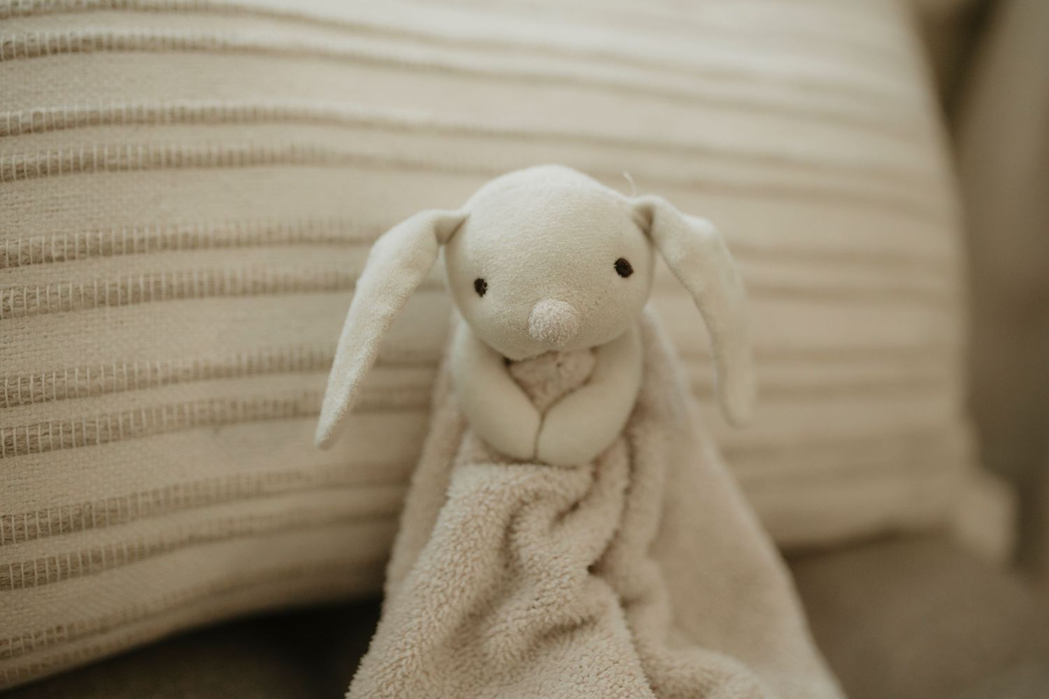 A white stuffed bunny plush toy sits against a beige ribbed fabric background.