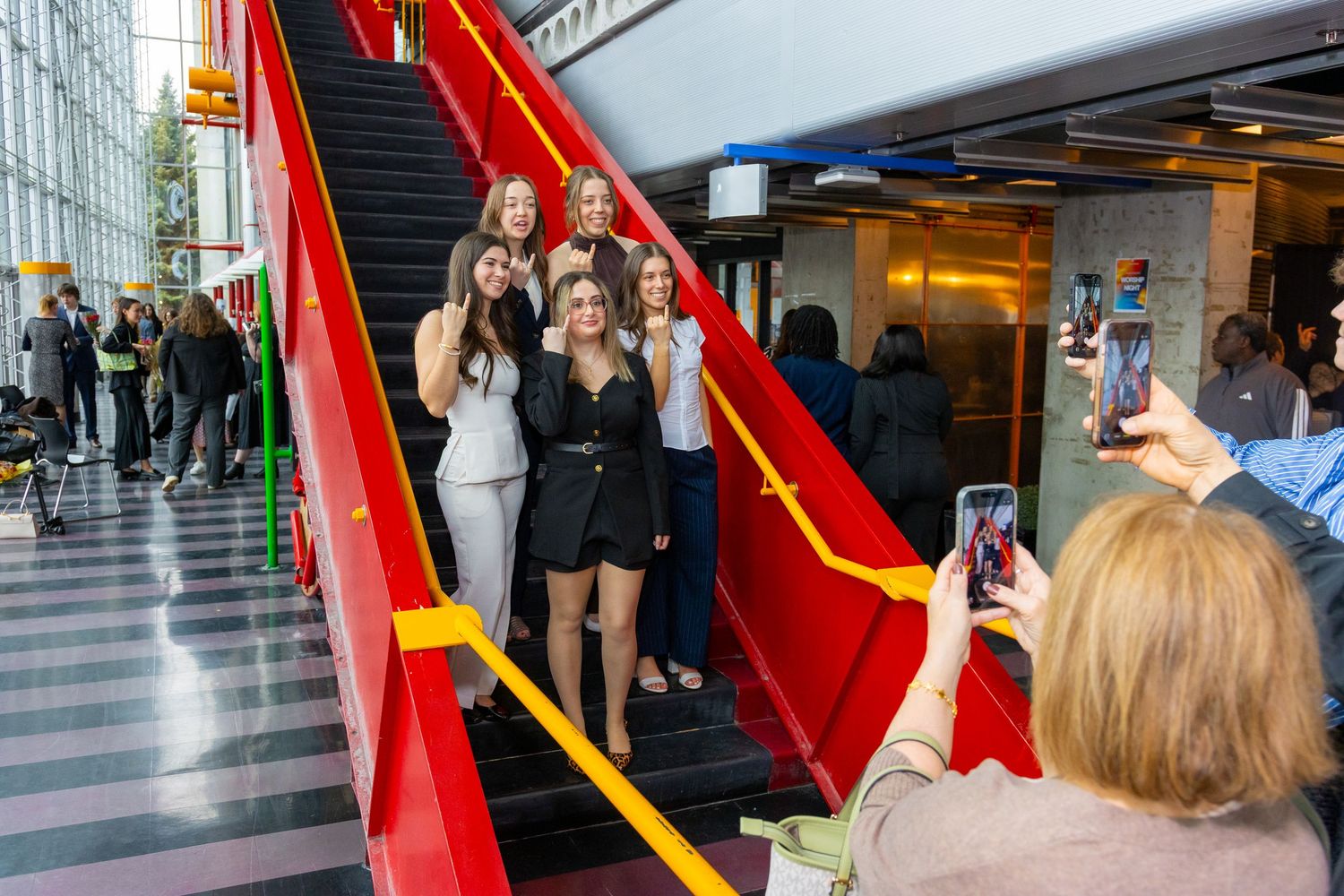 Group of young women posing for a photo on red escalator stairs inside a modern building.