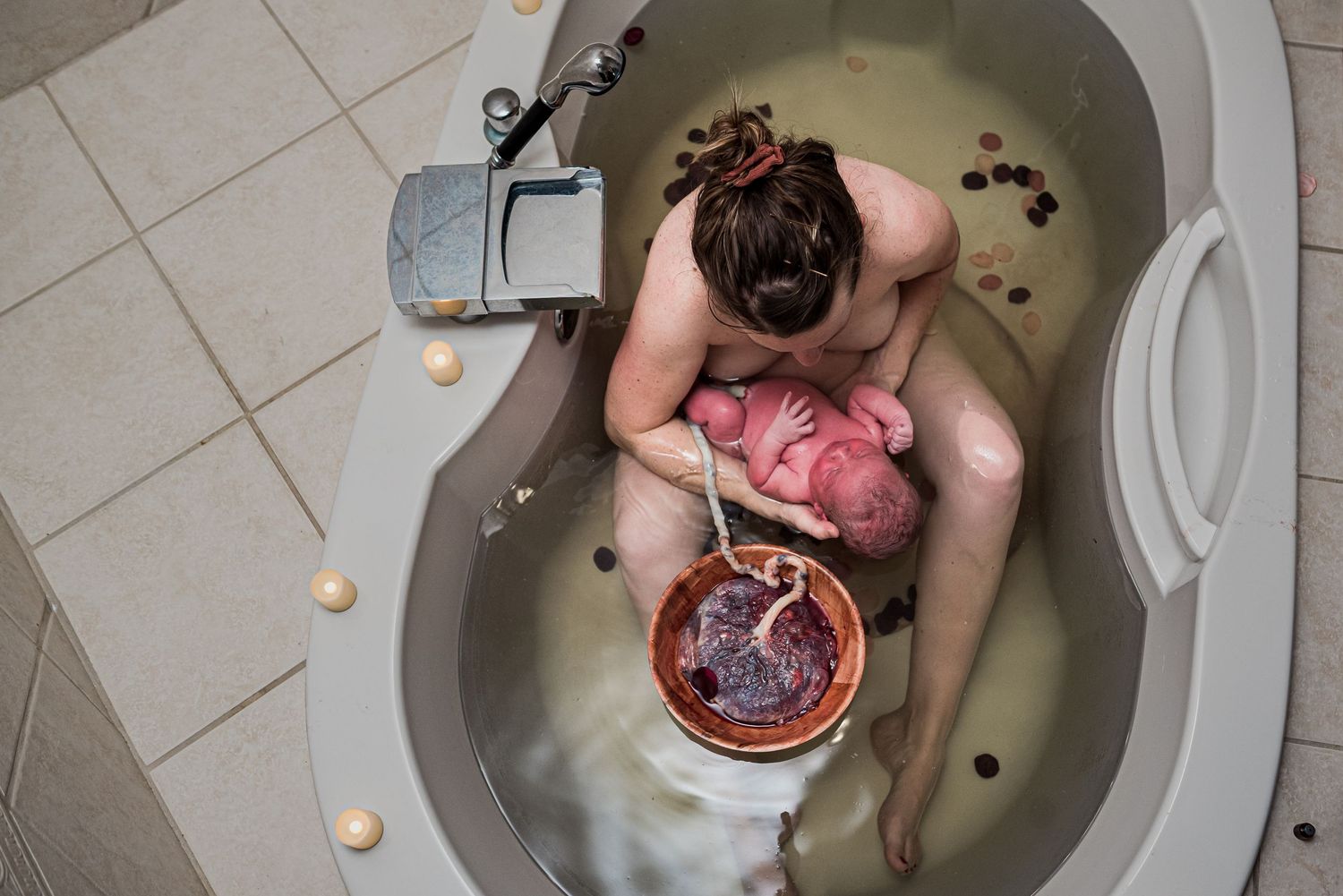 Mother holding newborn baby after water birth, kissing infant tenderly in bathtub during home birth.