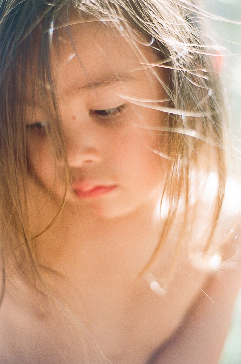 Ethereal close-up portrait with soft sunlight and wispy blonde hair.