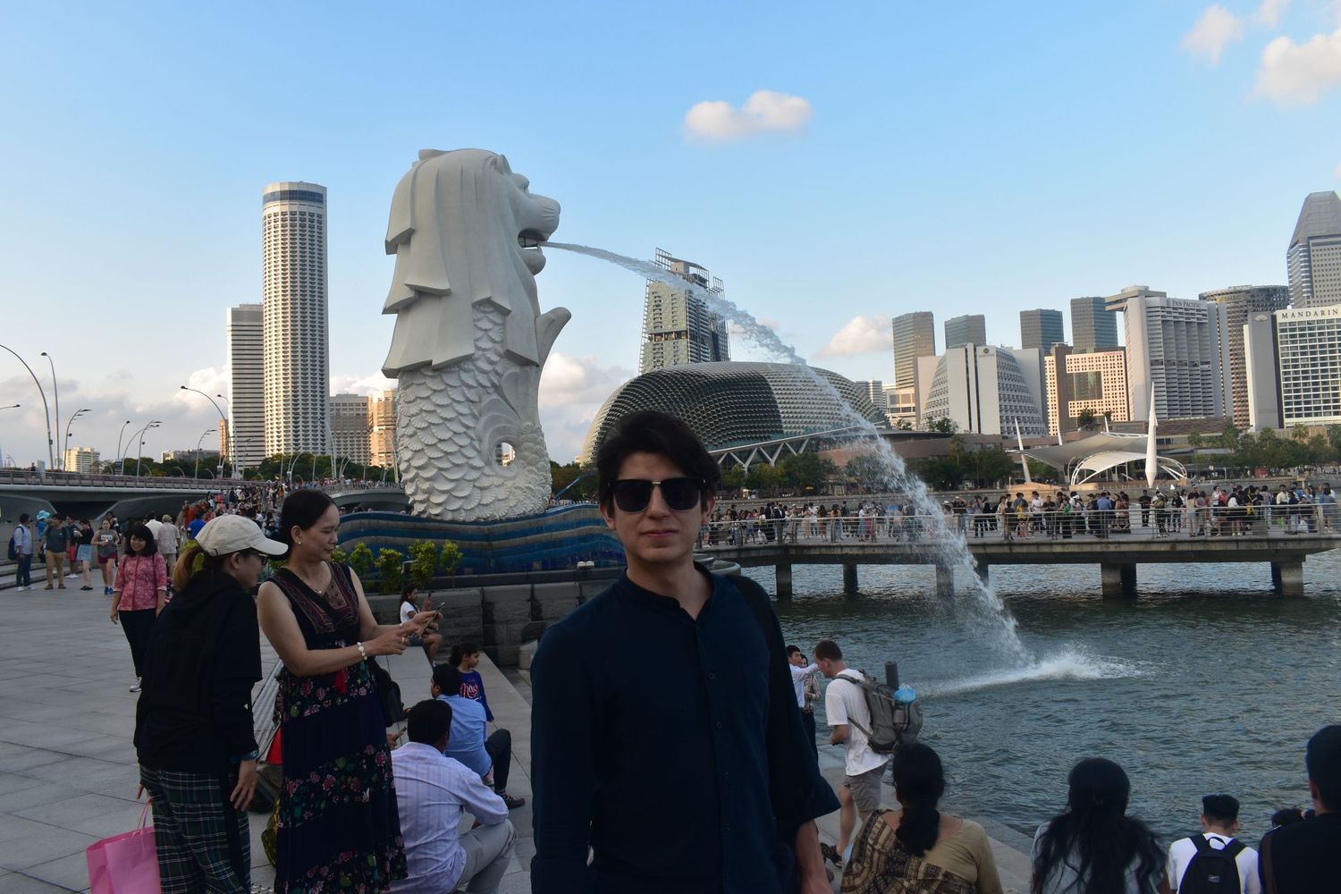 Tourist posing in front of the iconic Merlion fountain statue in Singapore with city skyline.
