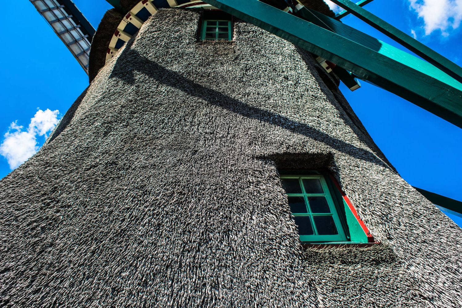 Low angle view of traditional Dutch windmill with thatched roof against blue sky.